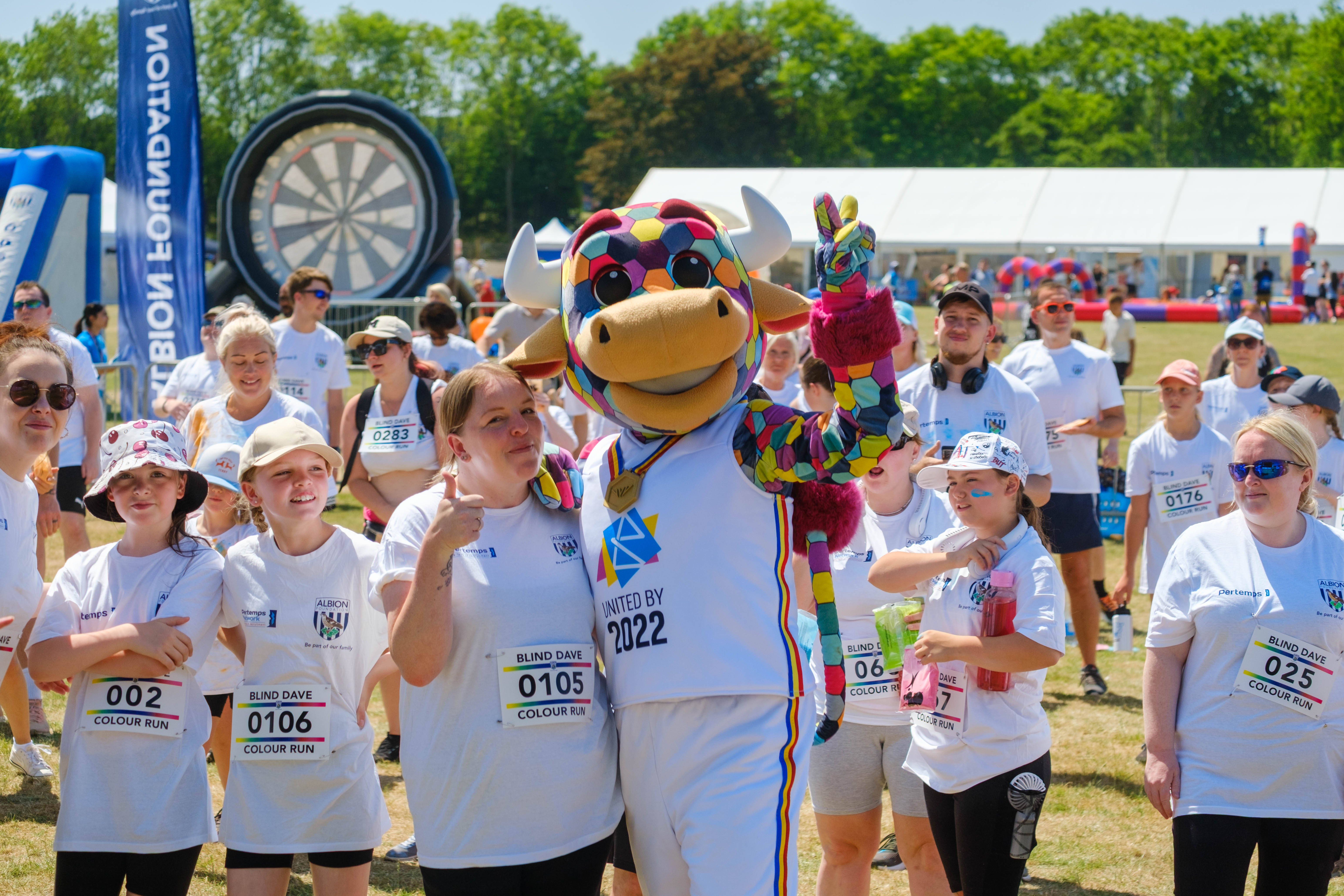 Perry the Bull with arm around a participant and thumb up, as the group pose for a photo.