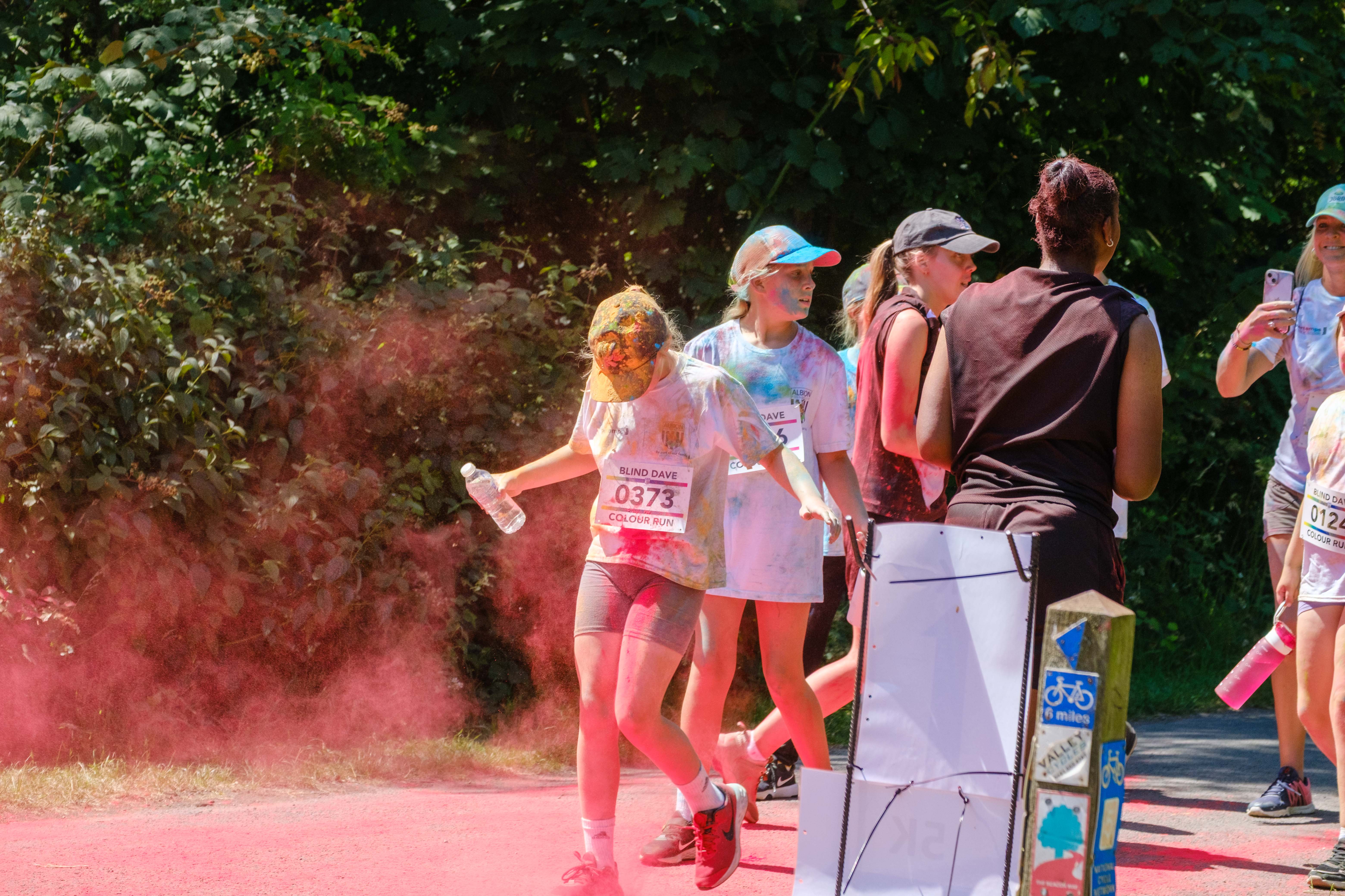 Runners passing colour station being douse with red powder.