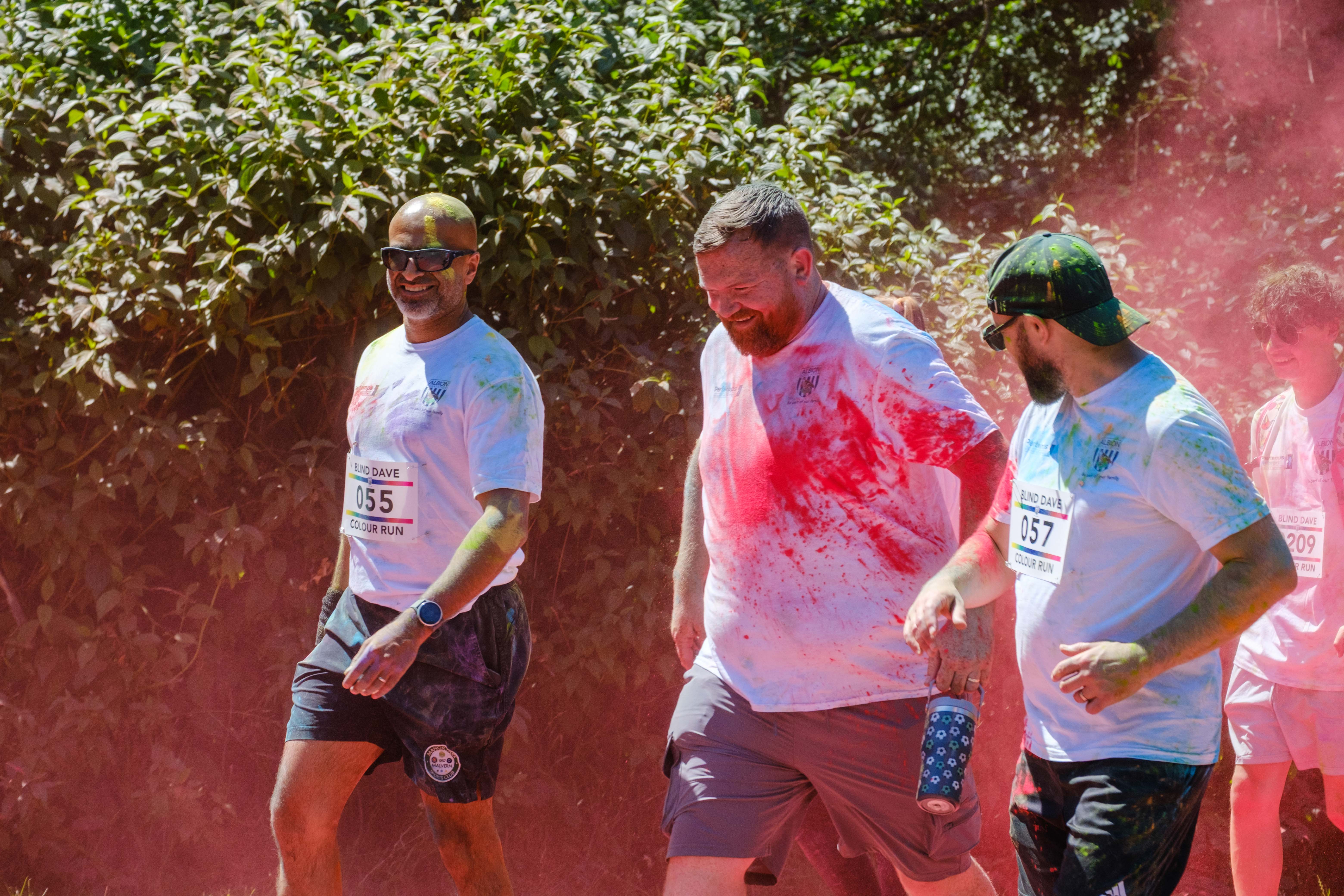 Runners passing colour station being douse with red powder.