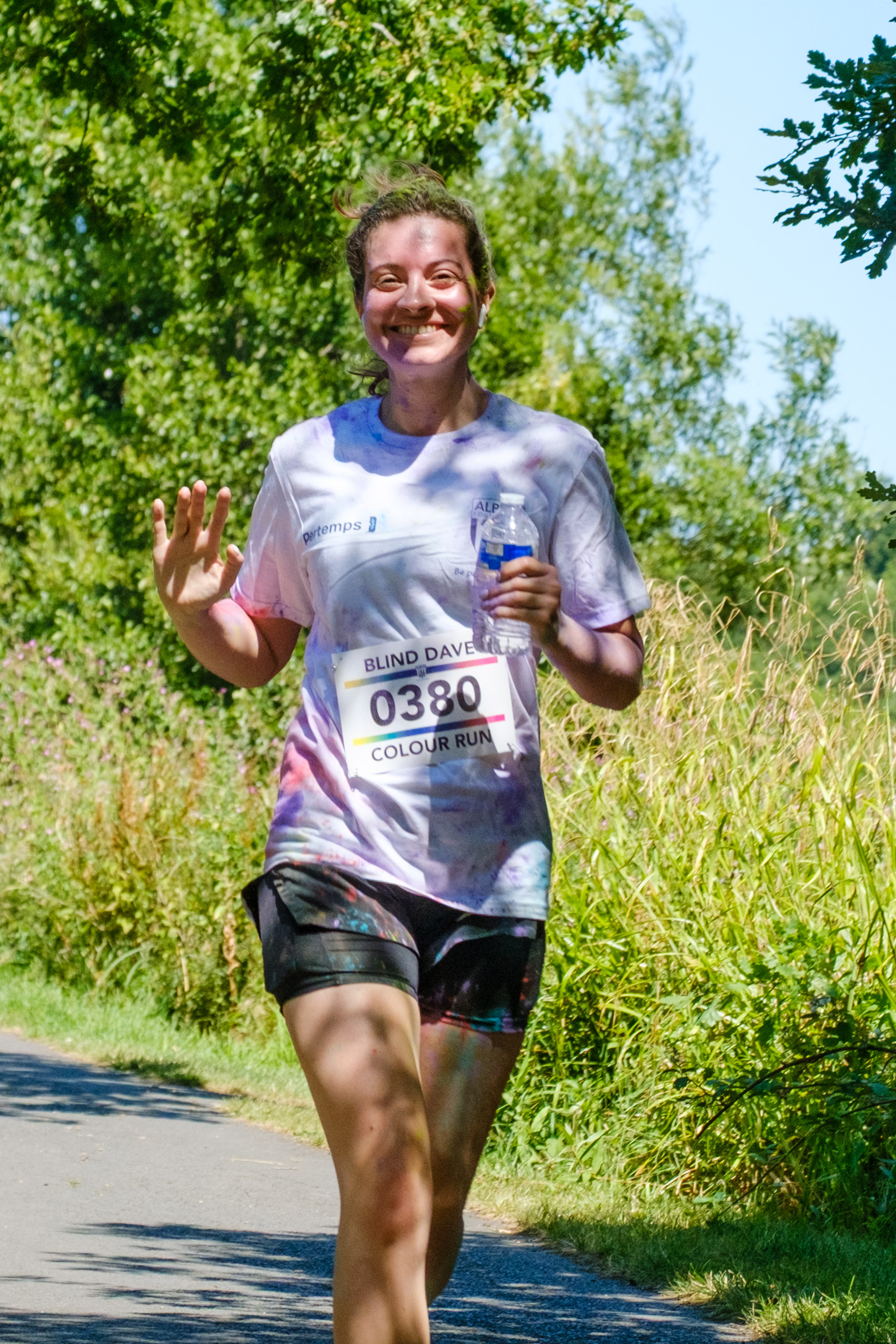 MP Sarah Coombe, waving and holding a bottle of water, as she running pass the pond.