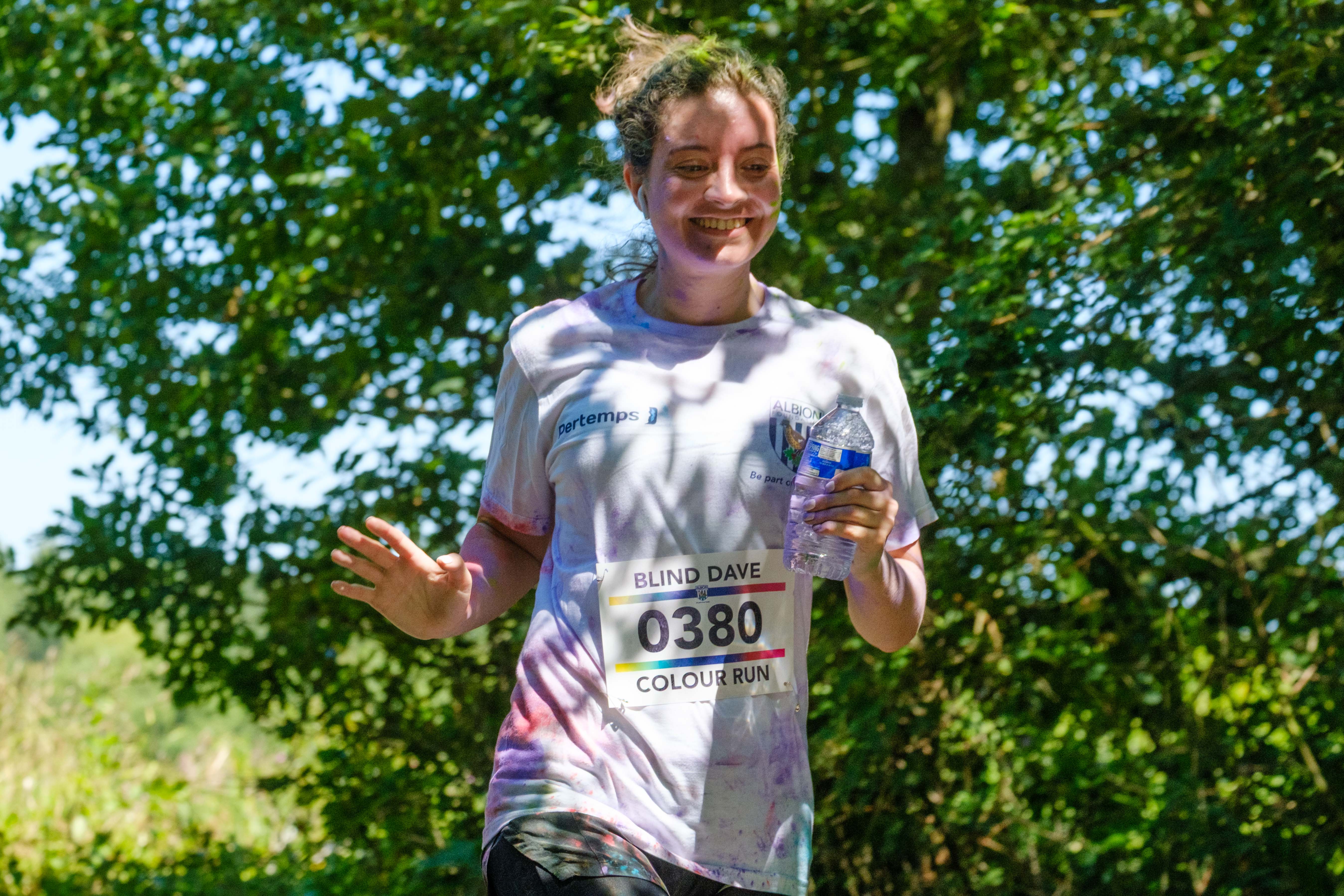 MP Sarah Coombe, waving and holding a bottle of water, as she running pass the pond.