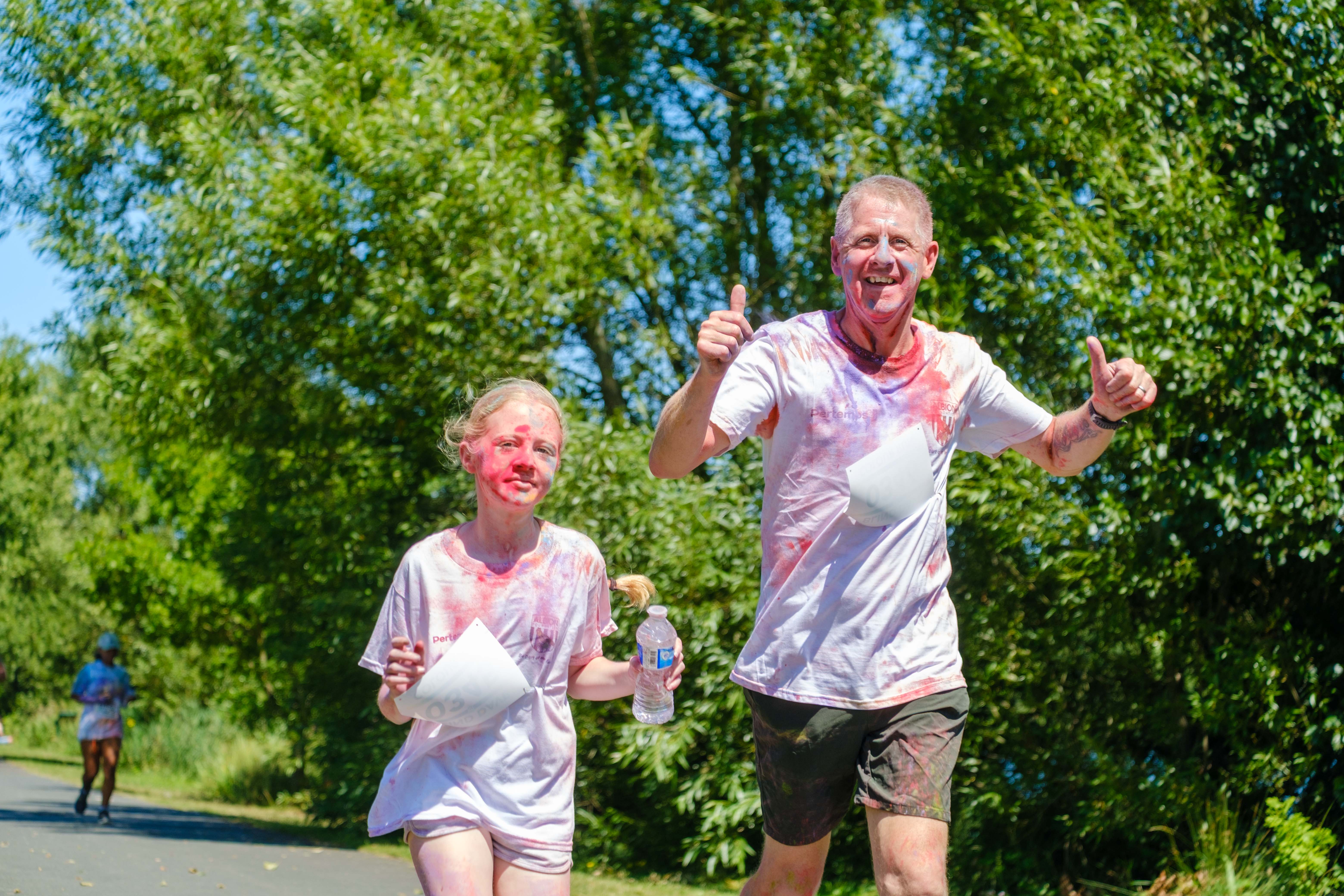 Father, with two thumbs up, and daughter running on the path.
