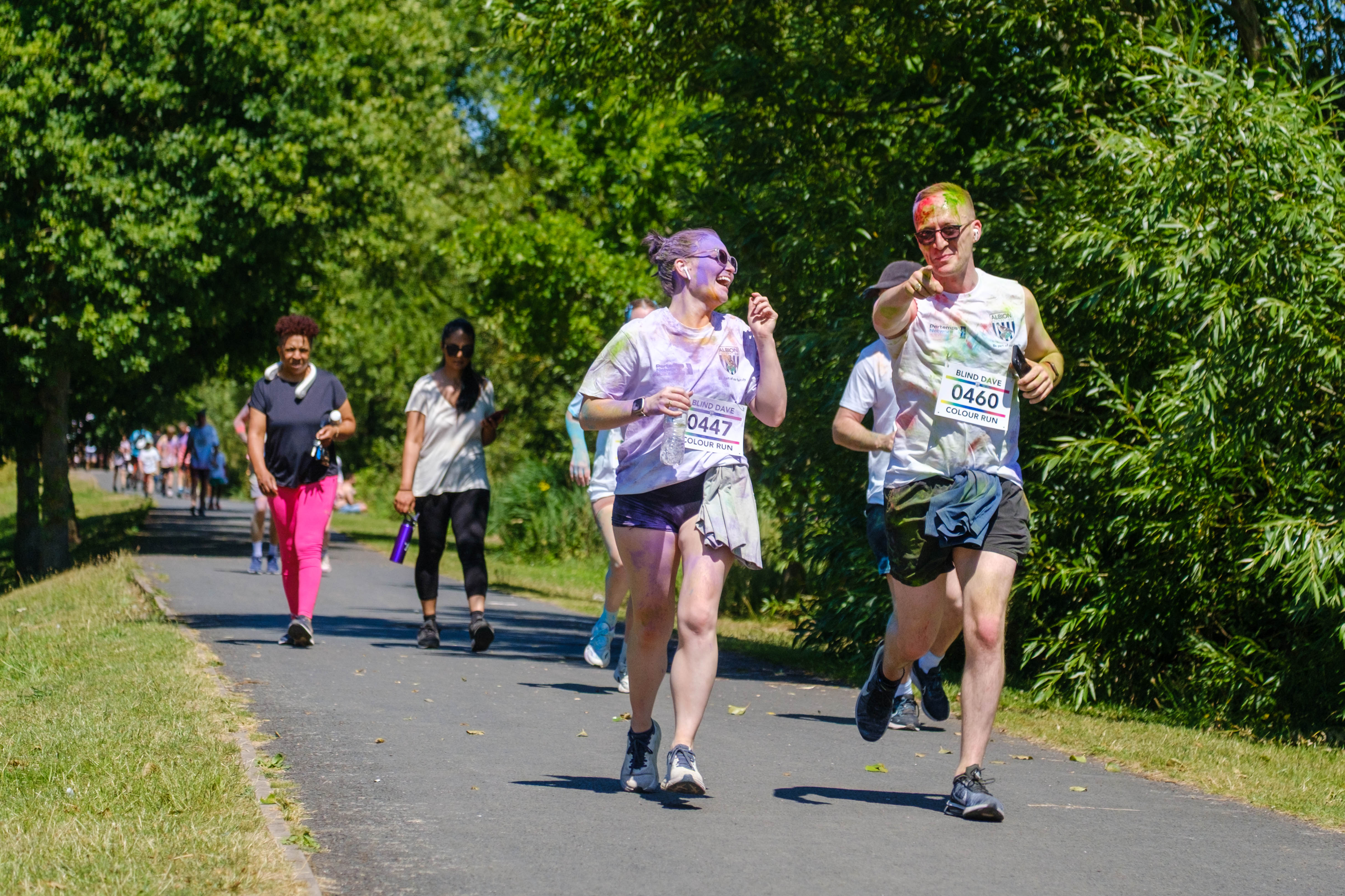 Man and woman running along the path. Woman is laughing while man is pointing at the camera.