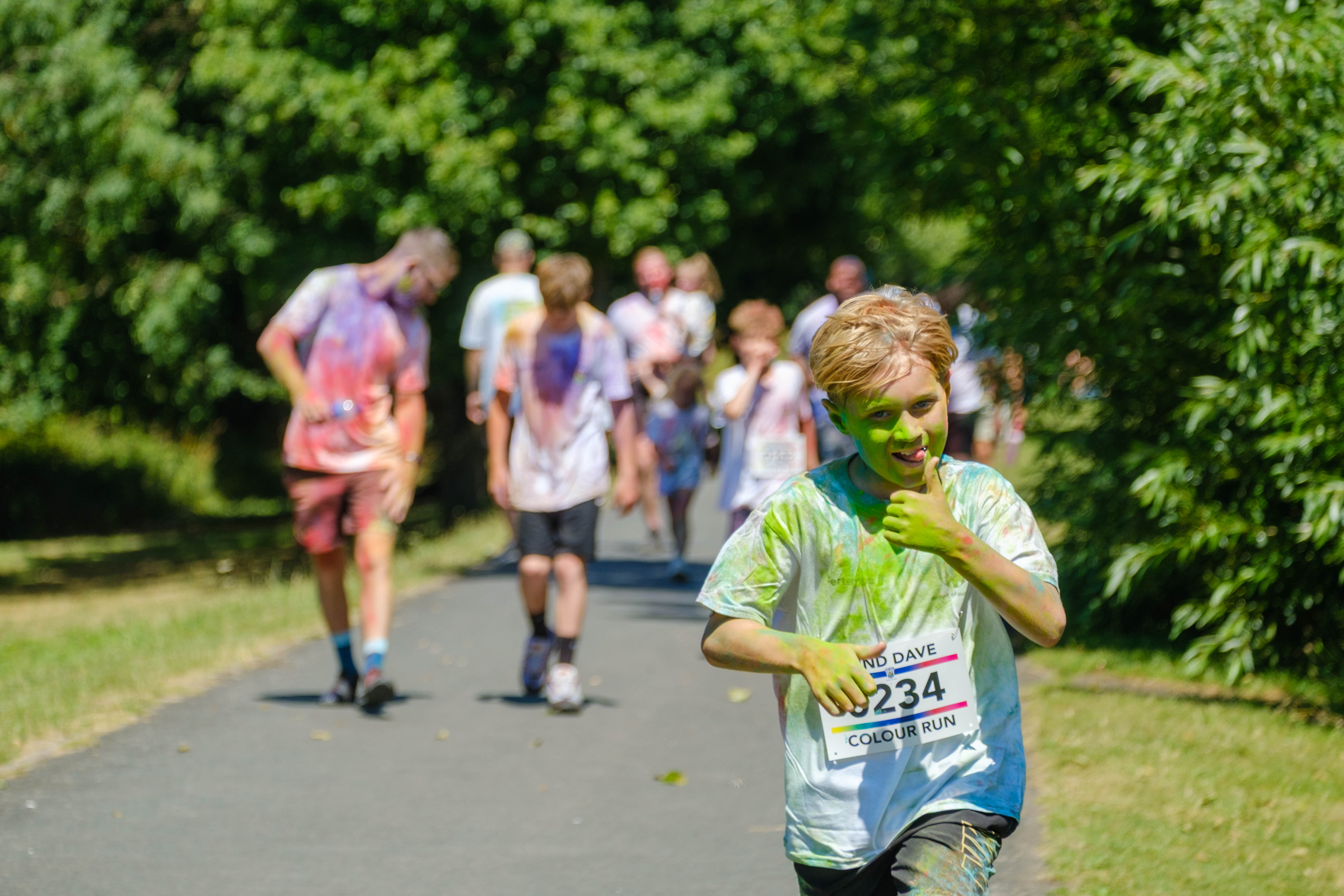 Young runner gives the thumbs up and tongue out, with group of runners in the background.