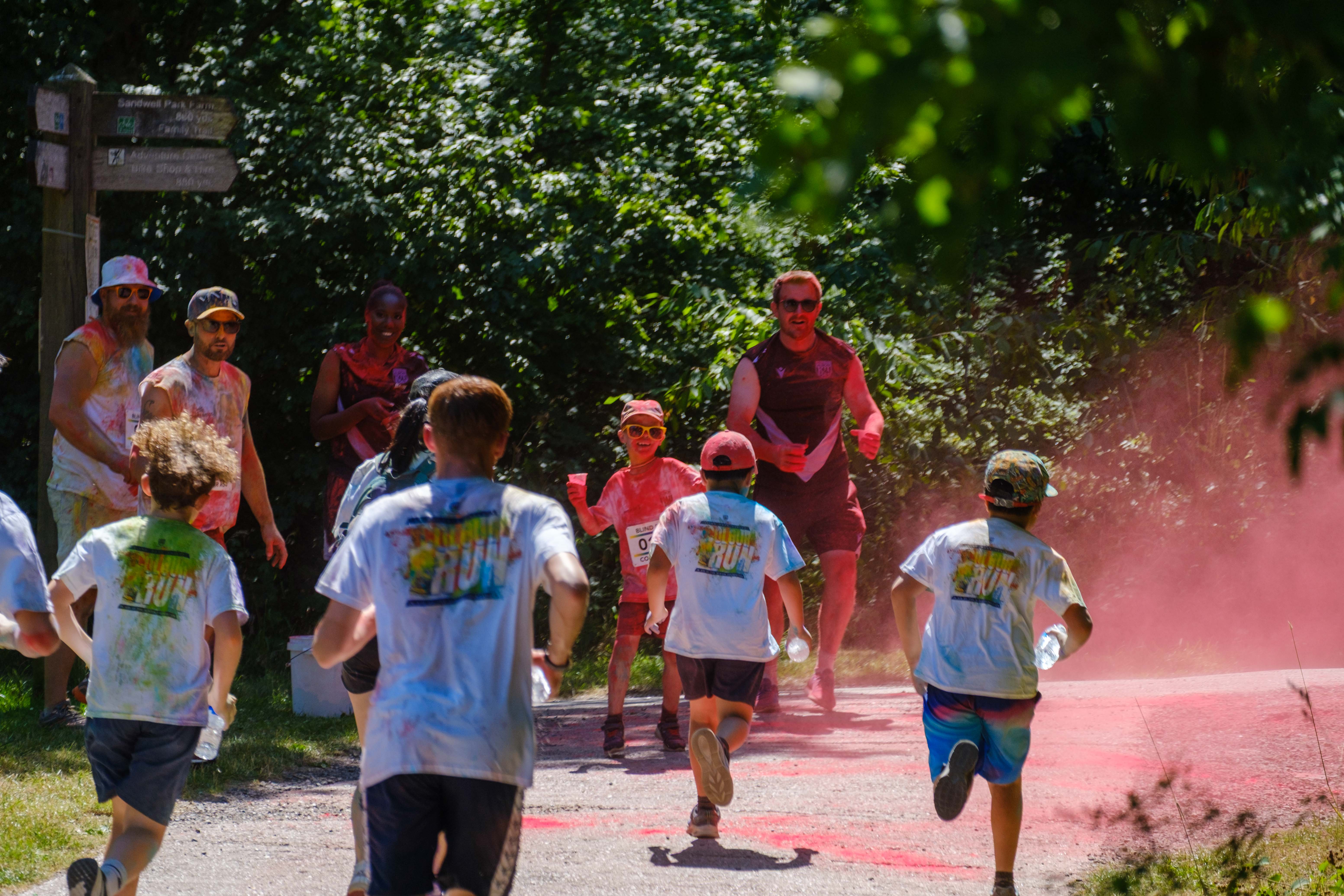 Group of five runners, heading towards a mist of red, with Foundation staff and volunteers waiting to douse them with paint.