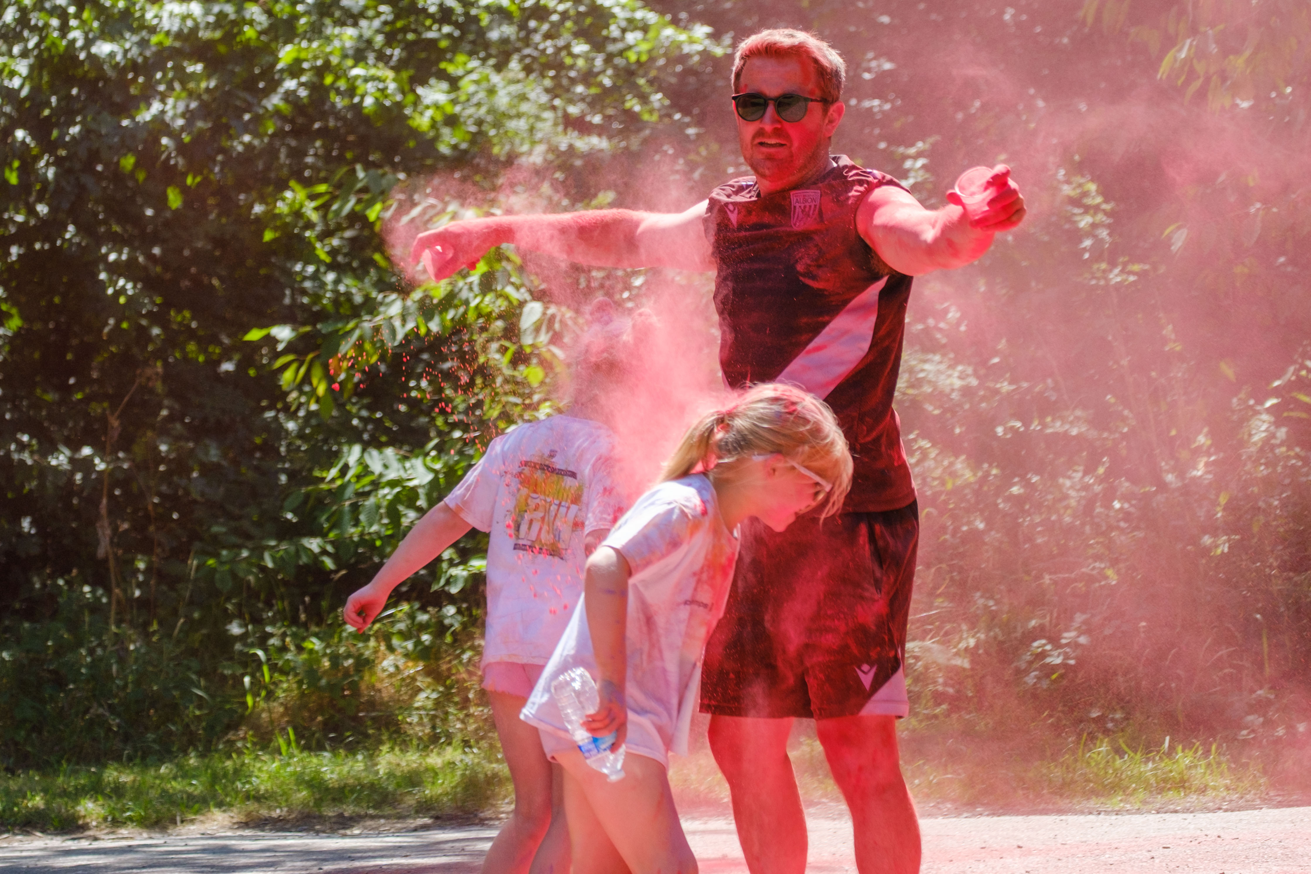 Young runners running under the arms of Foundation staff as he releases red paint.