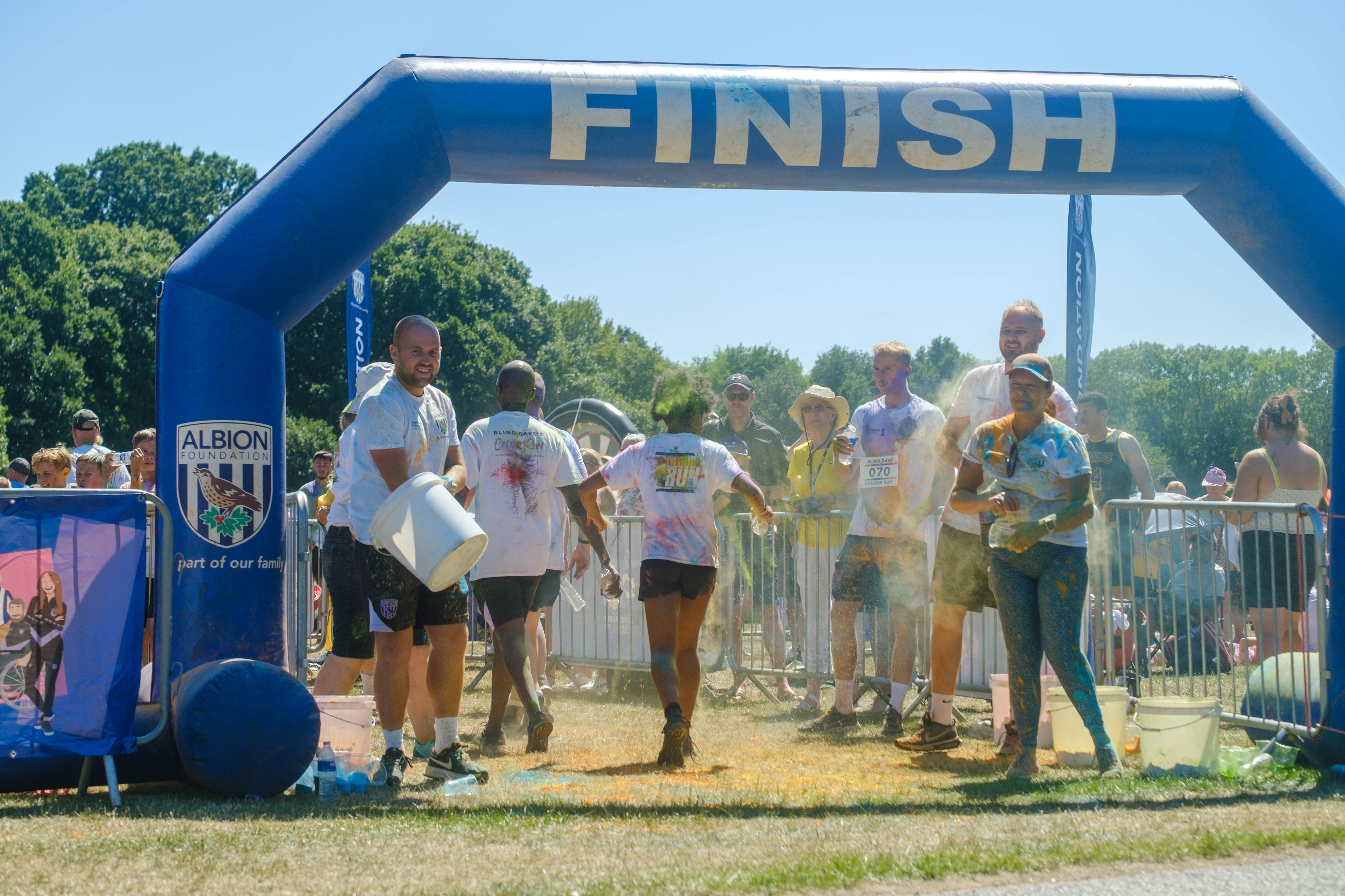 Runners crossing the finish line, as staff and volunteers throw paint.