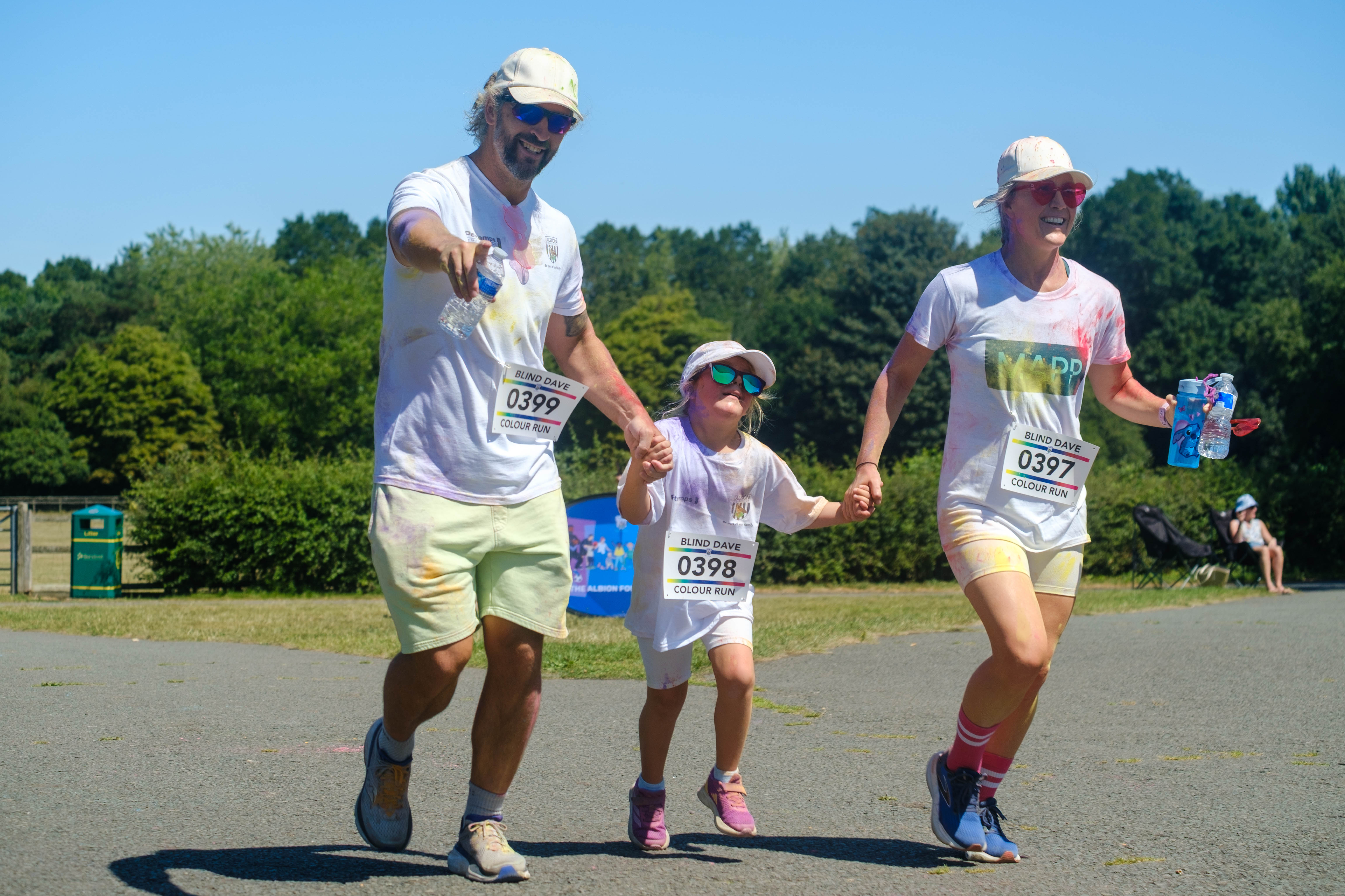 Parents and child holding hands running towards the finish, father pointing at the camera. 