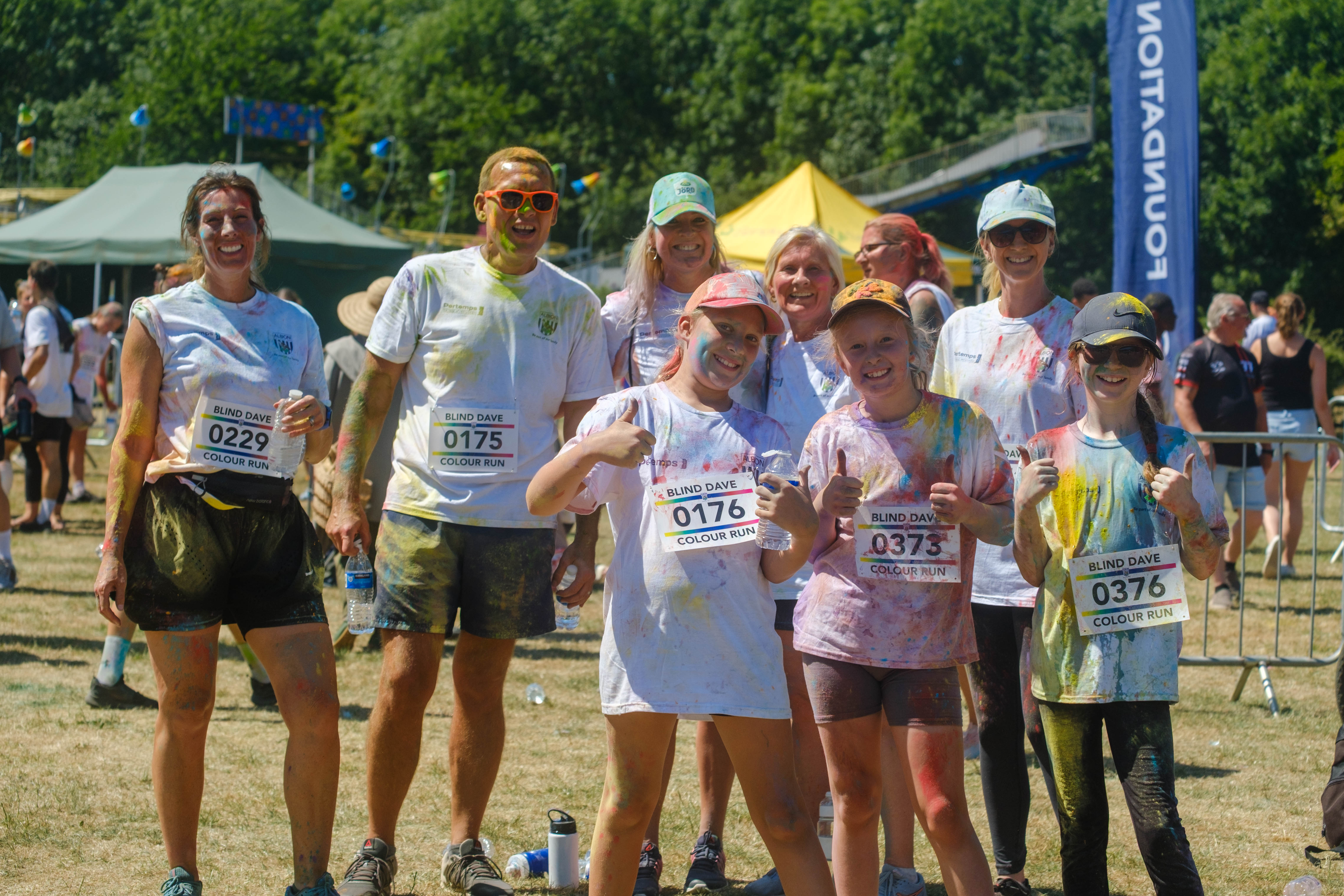 Mixture group adults and children smiling and thumbs up after completing the Colour Run.