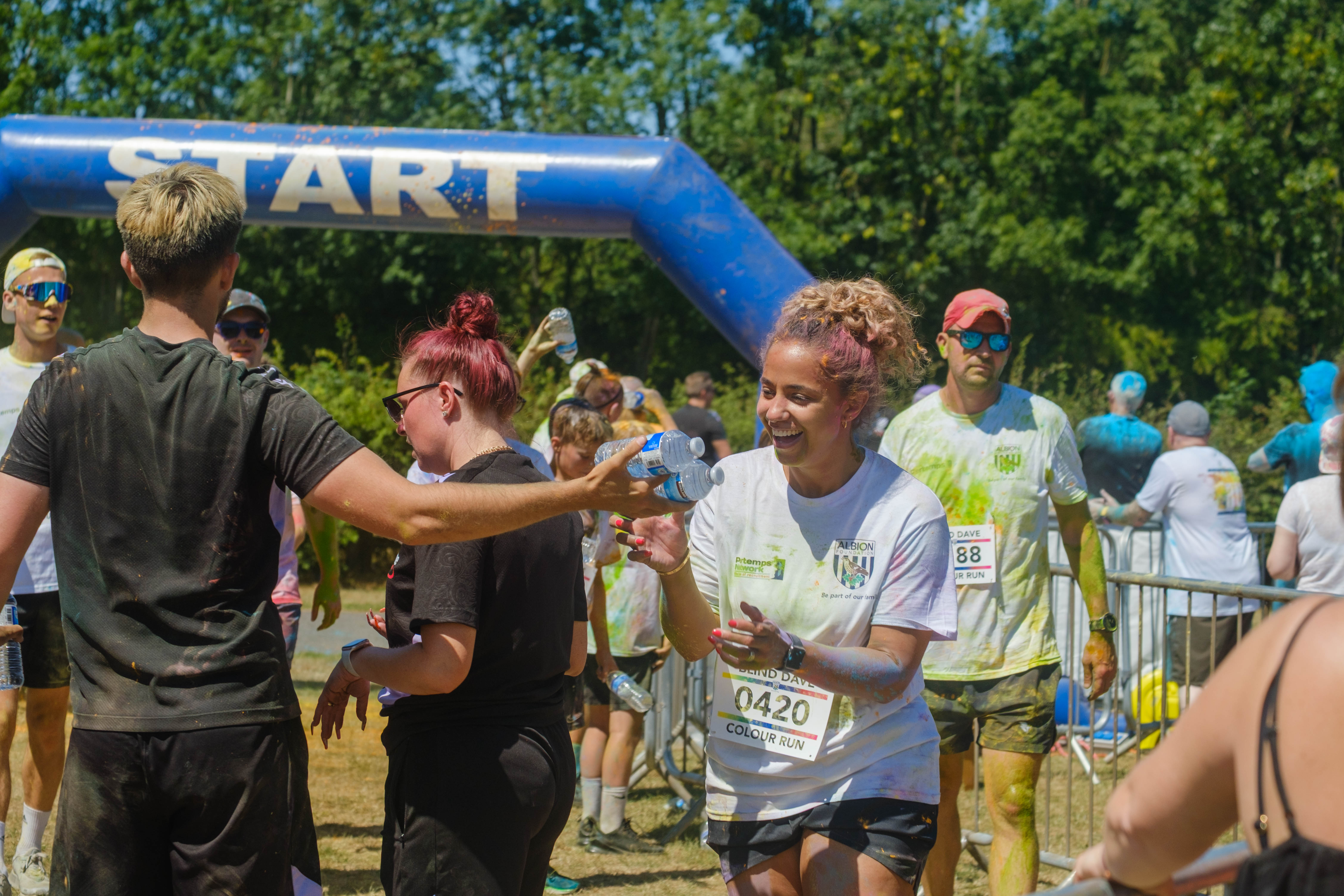 Runner 0420 smiling, as she is handed a bottle of water from Foundation staff at the end of the run.