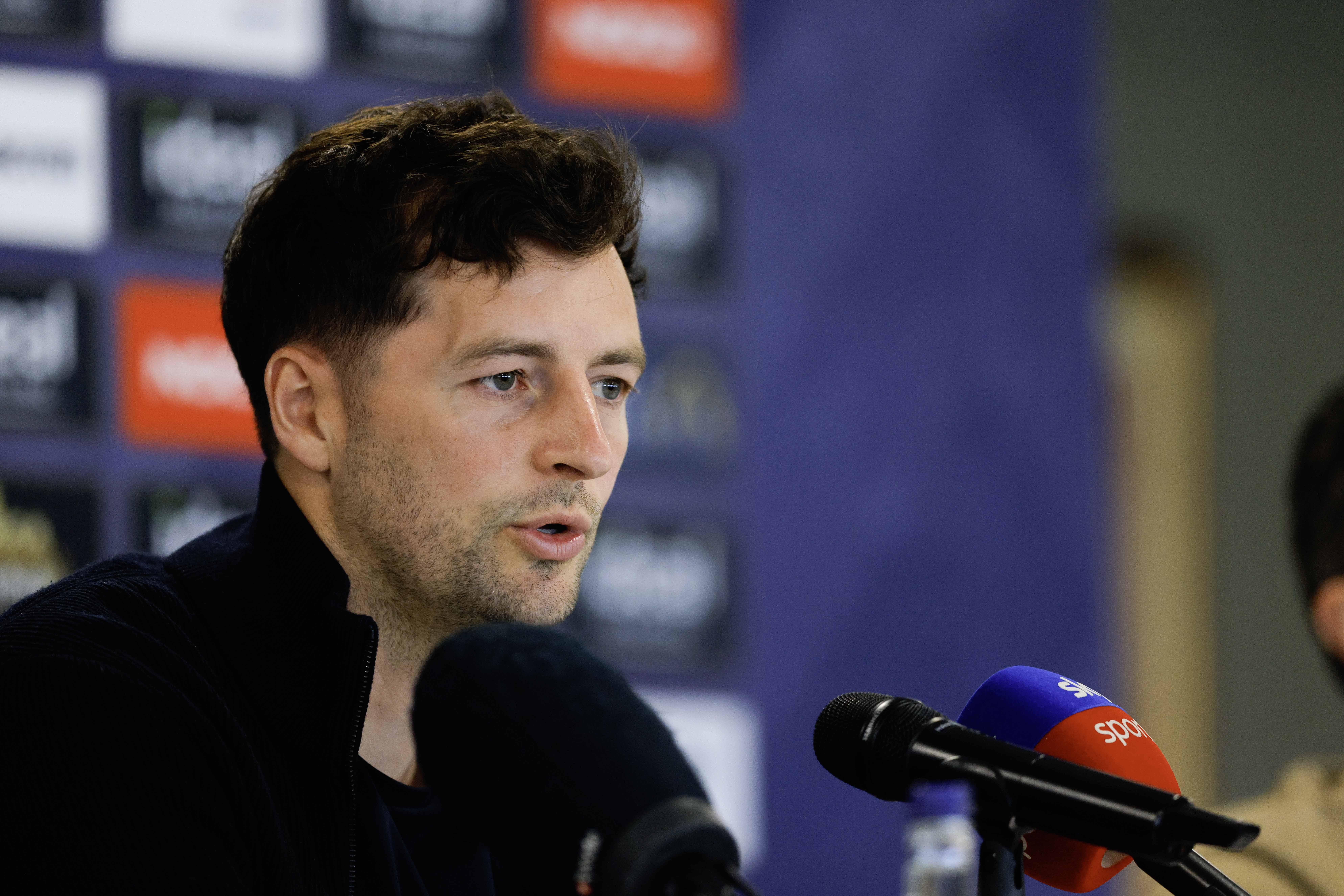 Ryan Mason talking to members of the media in front of a press conference sponsor board and behind a number of microphones