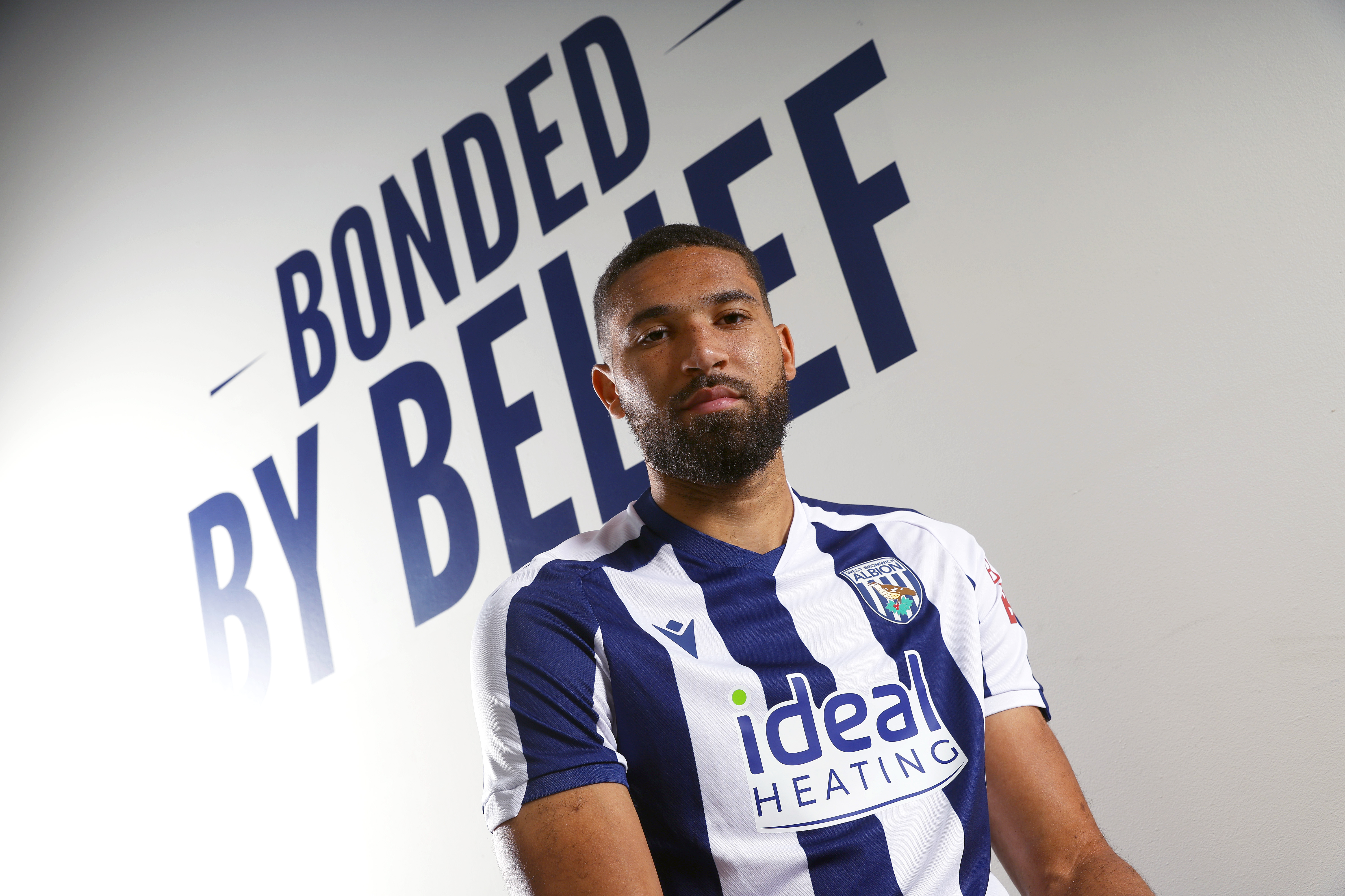 George Campbell sat looking at the camera with 'Bonded by belief' branding written on the wall behind him