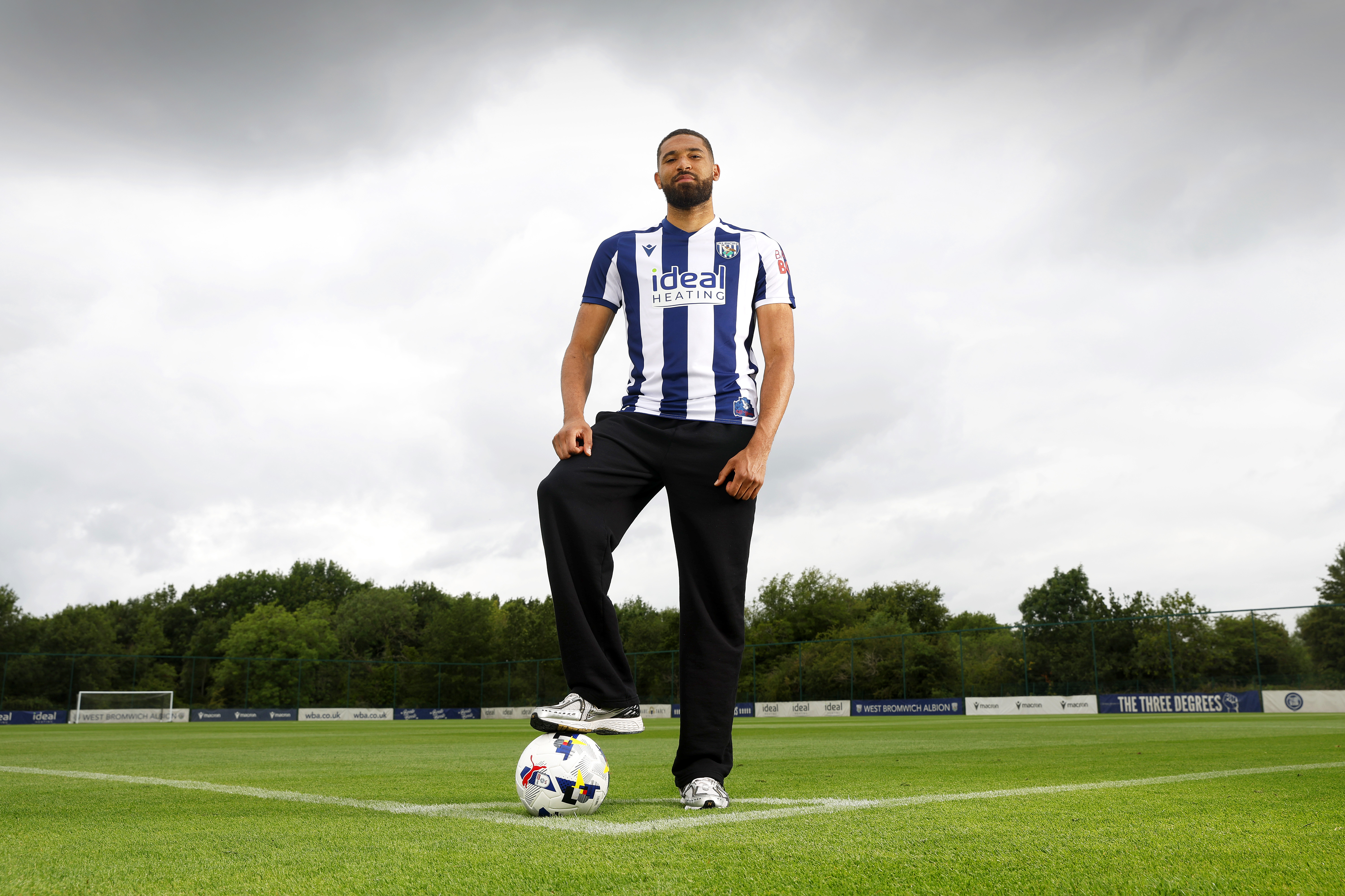 George Campbell stood in the middle of a training pitch in a home WBA shirt with his foot on a ball while smiling at the camera 