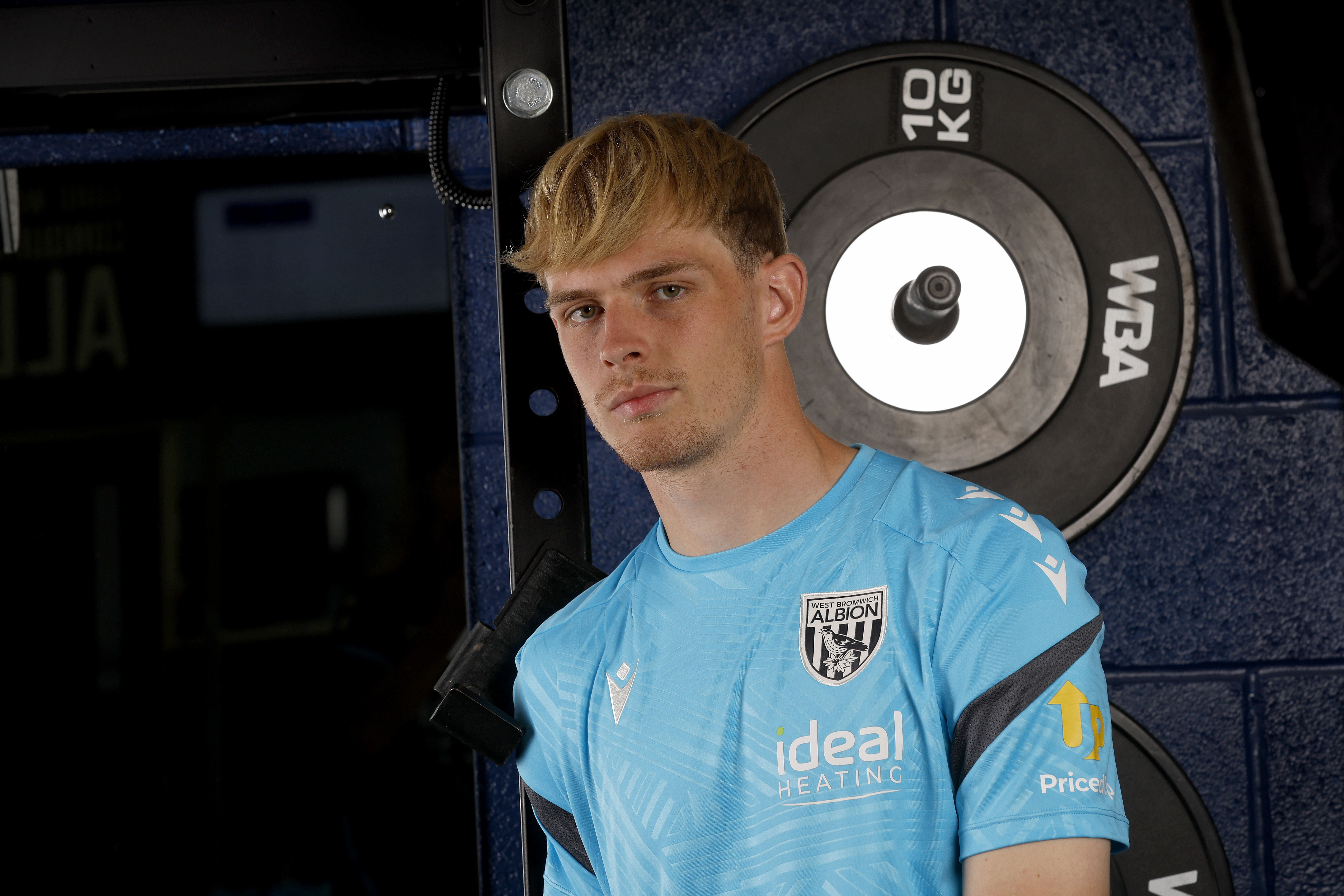 Toby Collyer looking at the camera while stood in front of weights in the gym