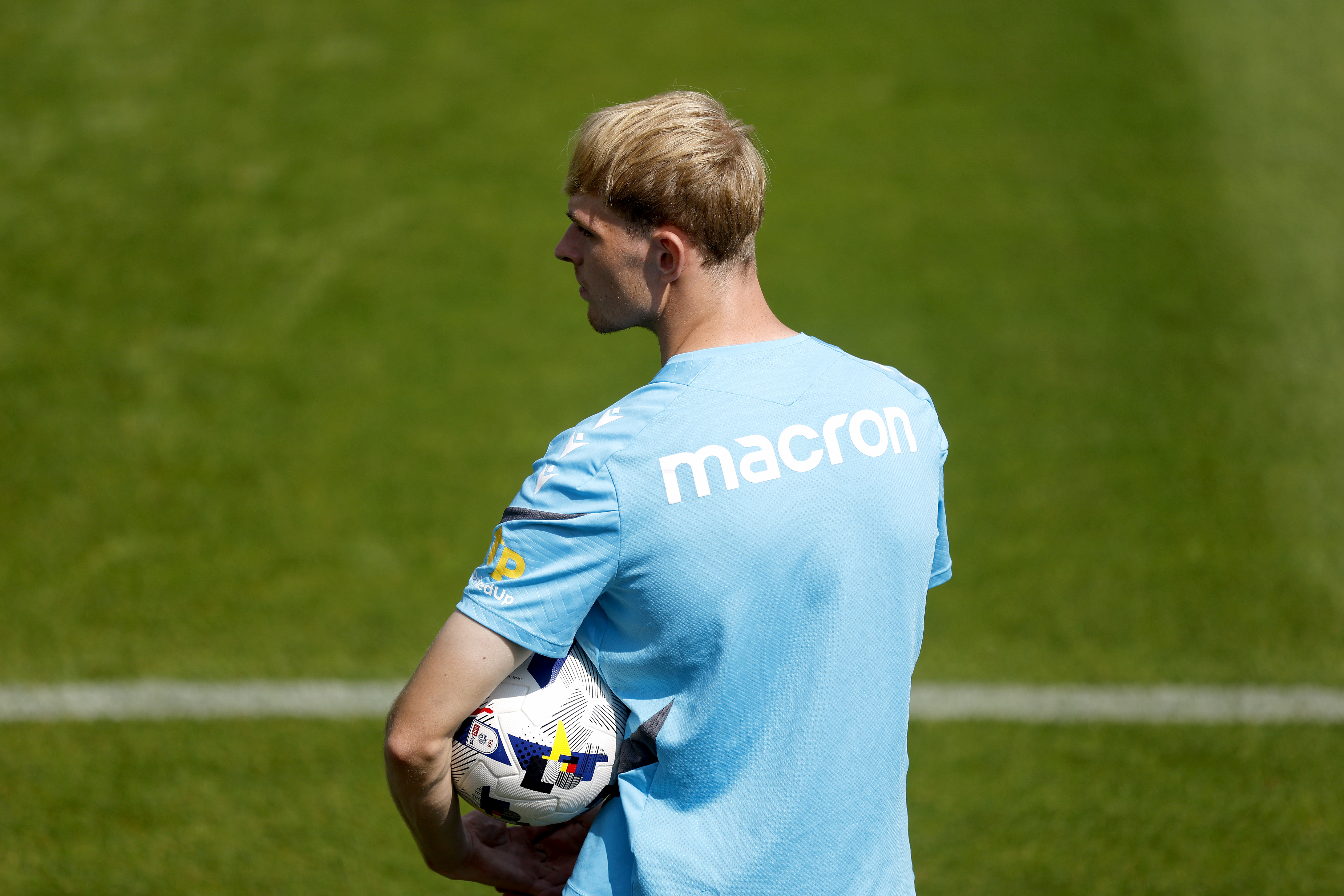 Toby Collyer holding a ball watching training with his back to the camera 