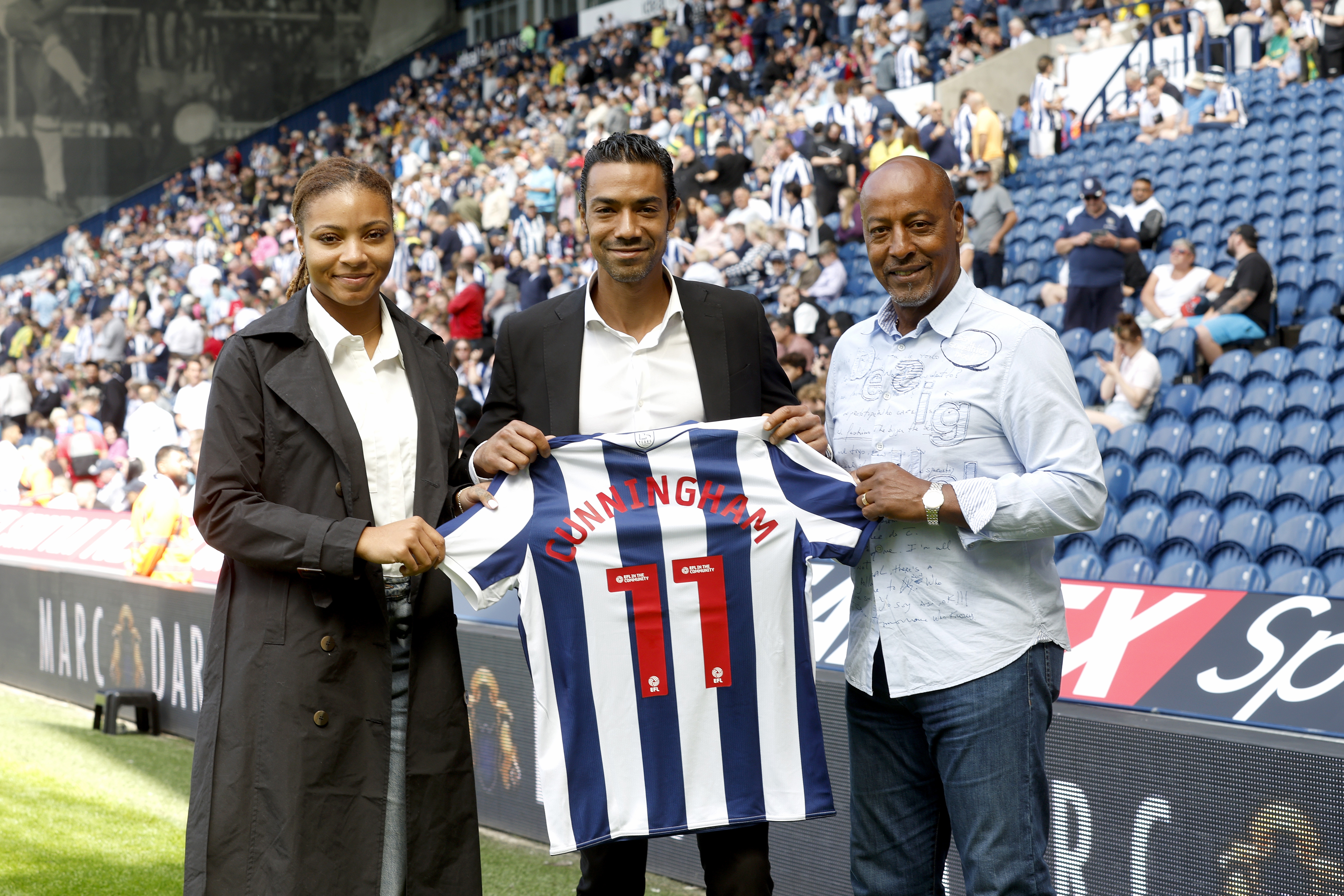 Jayda Regis, Sergio Cunningham and Brendon Batson holding up a WBA shirt with 'Cunningham 11' on the back