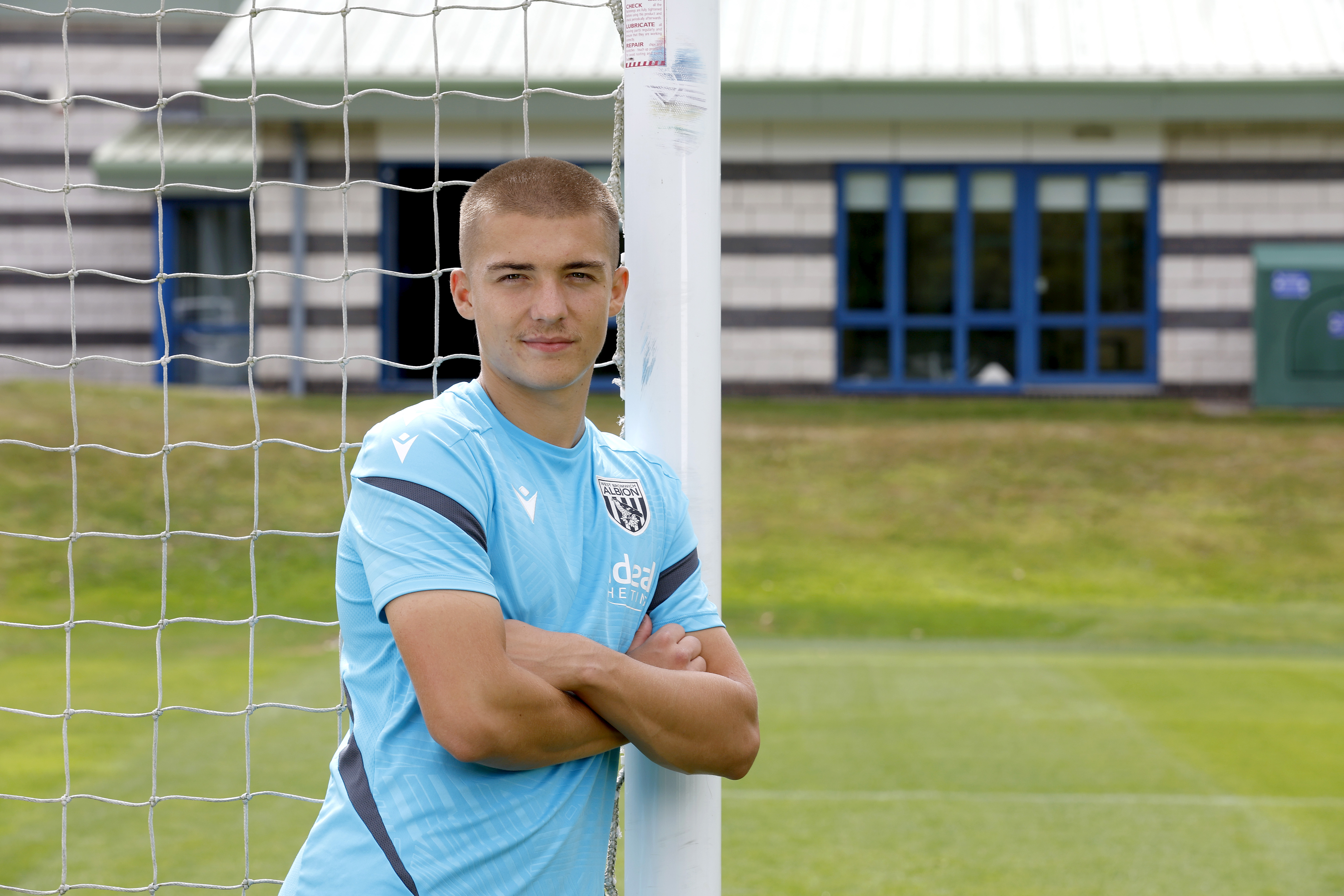 Alfie Gilchrist with his arms folded leaning up against a goal post