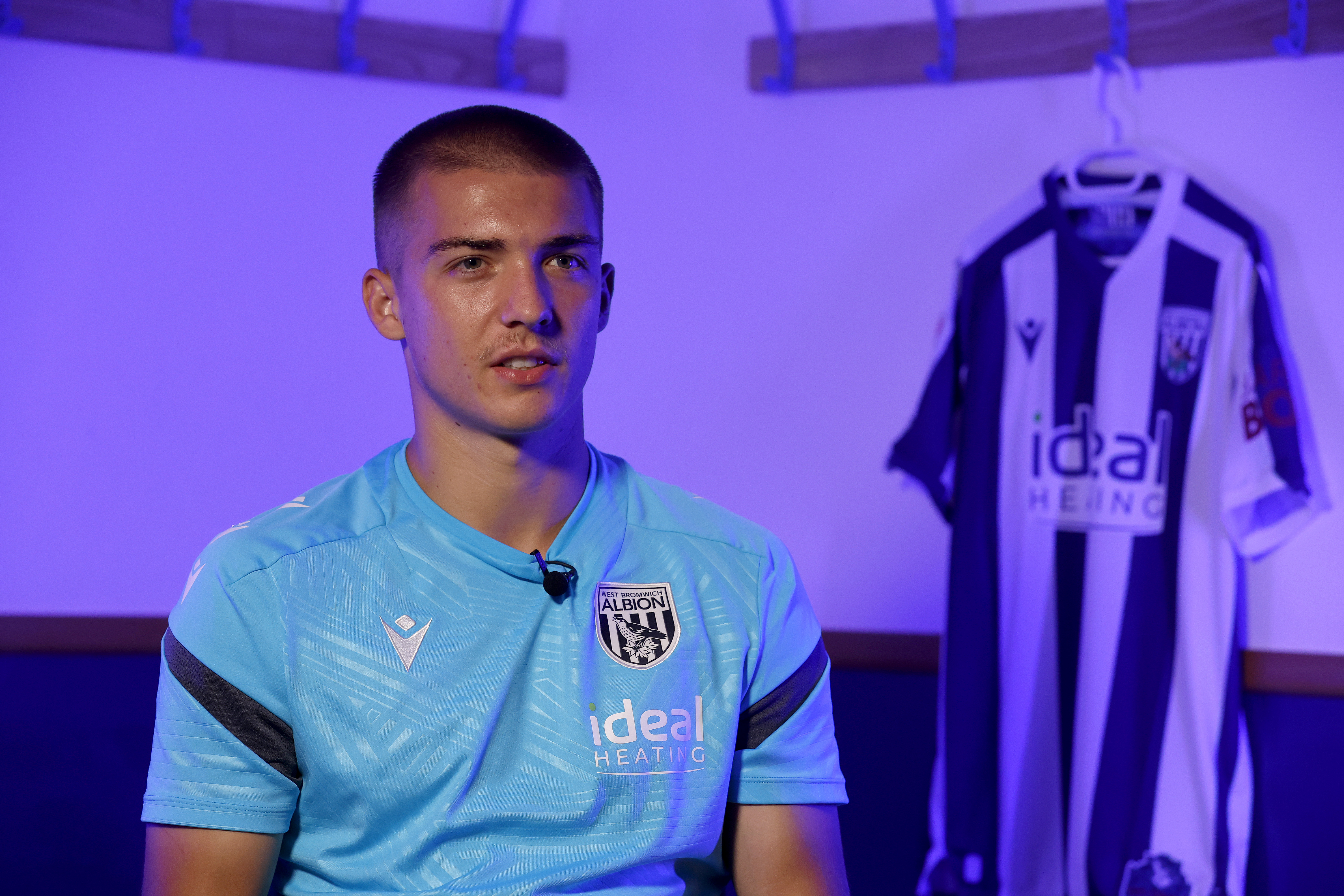 Alfie Gilchrist speaking to WBA TV with a WBA home shirt in the background hanging up