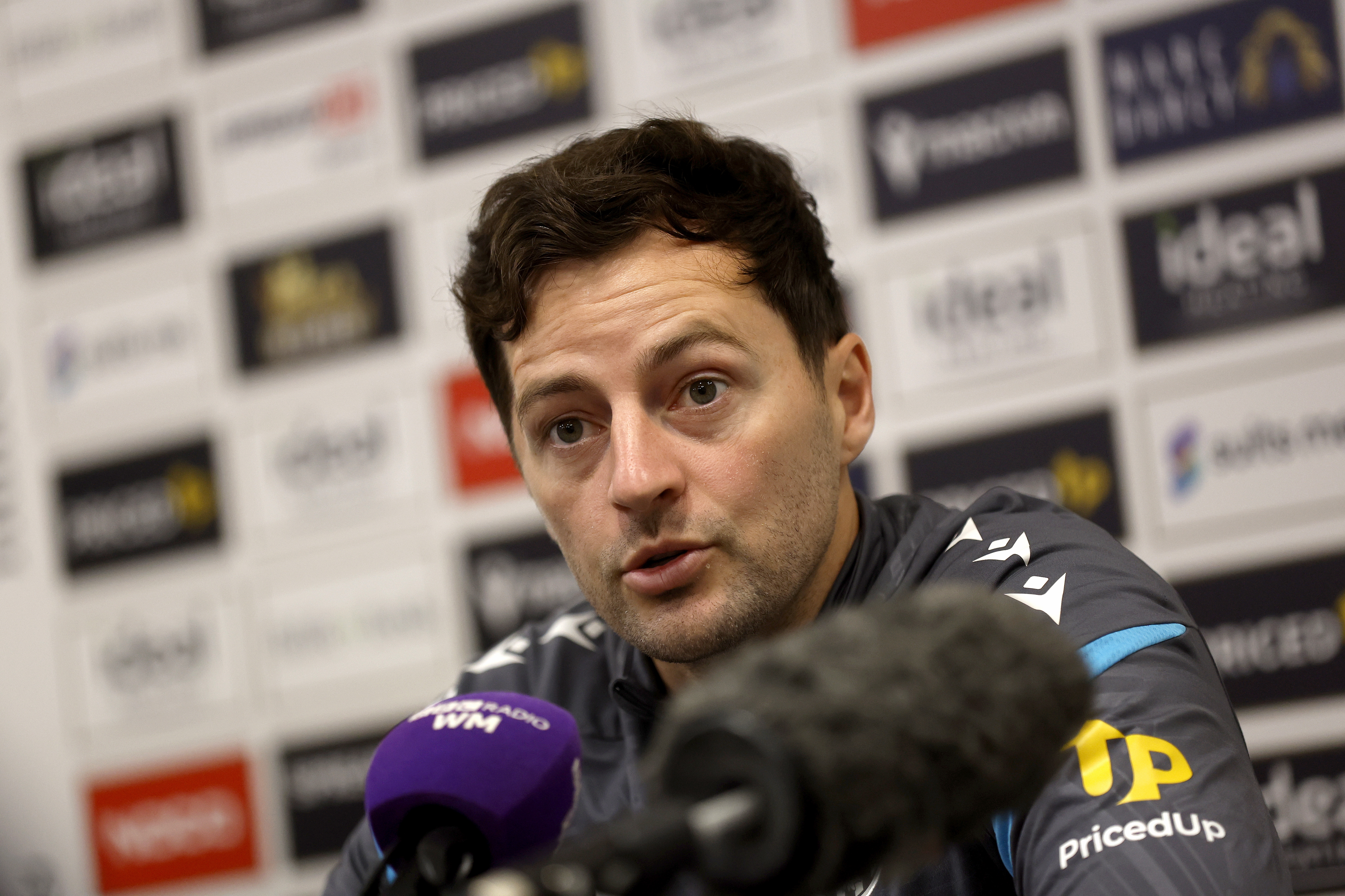 Ryan Mason speaking to press in front of a sponsors board