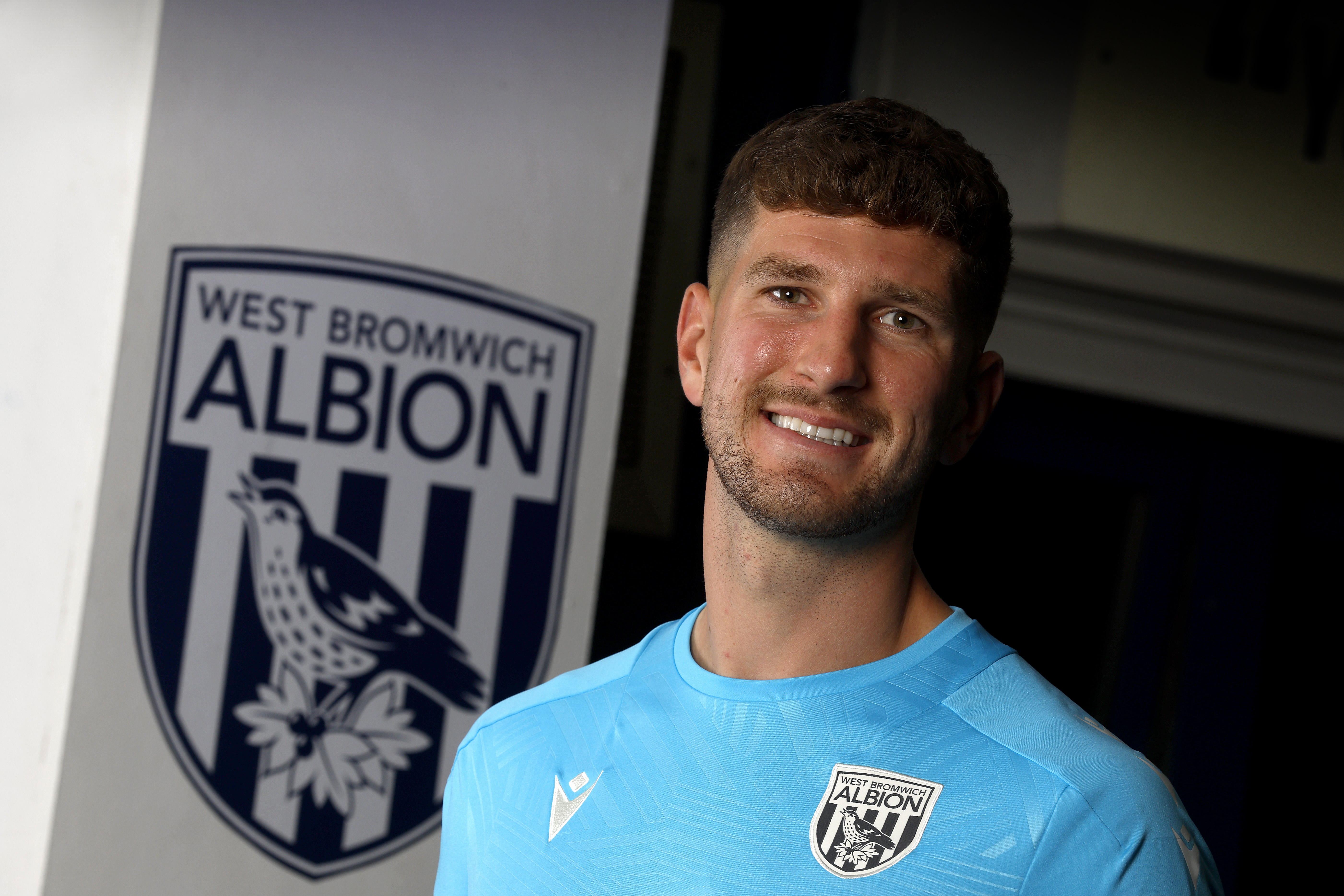 Chris Mepham stood by an Albion badge smiling and looking at the camera