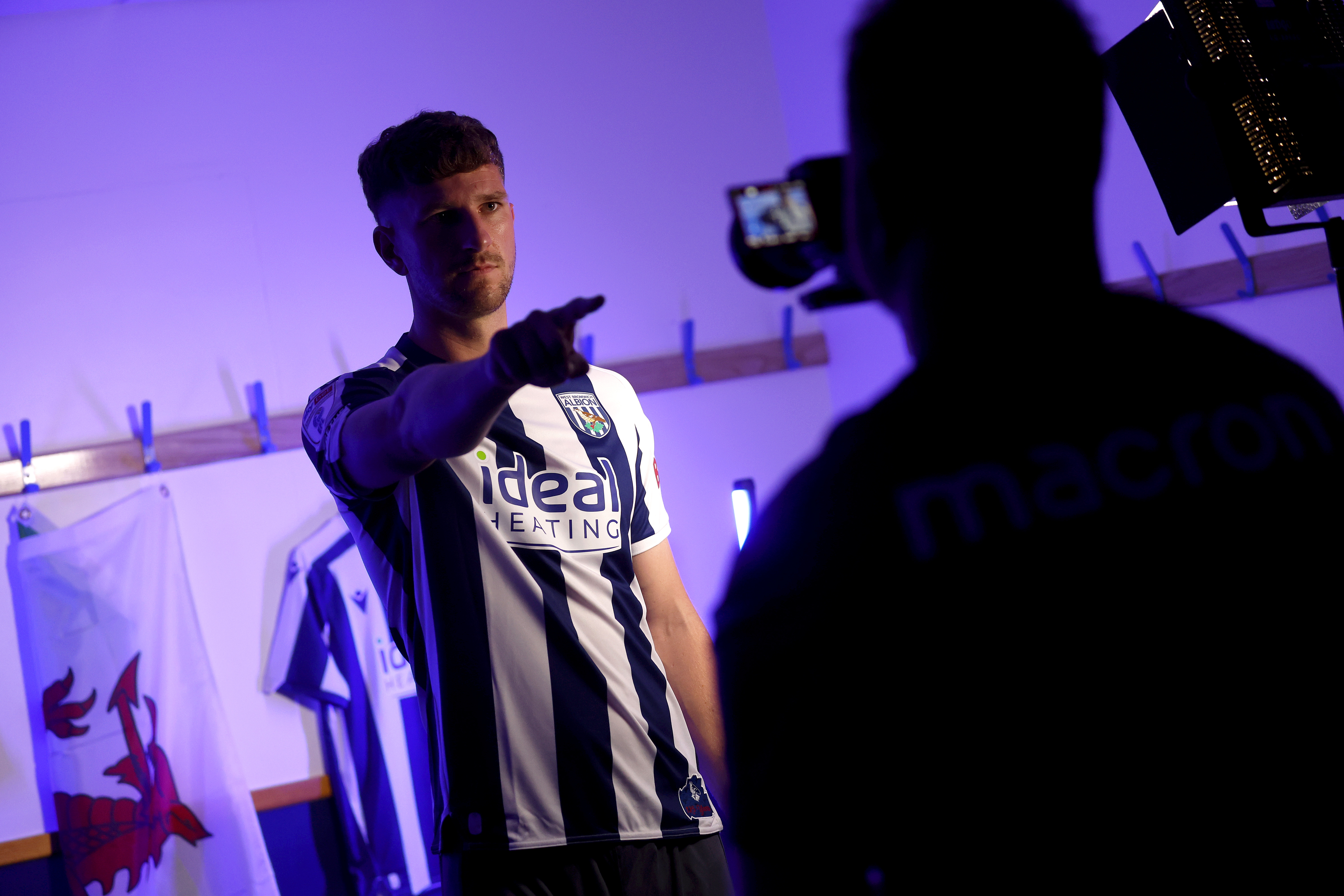 Chris Mepham being filmed pointing at a camera while wearing a home WBA shirt