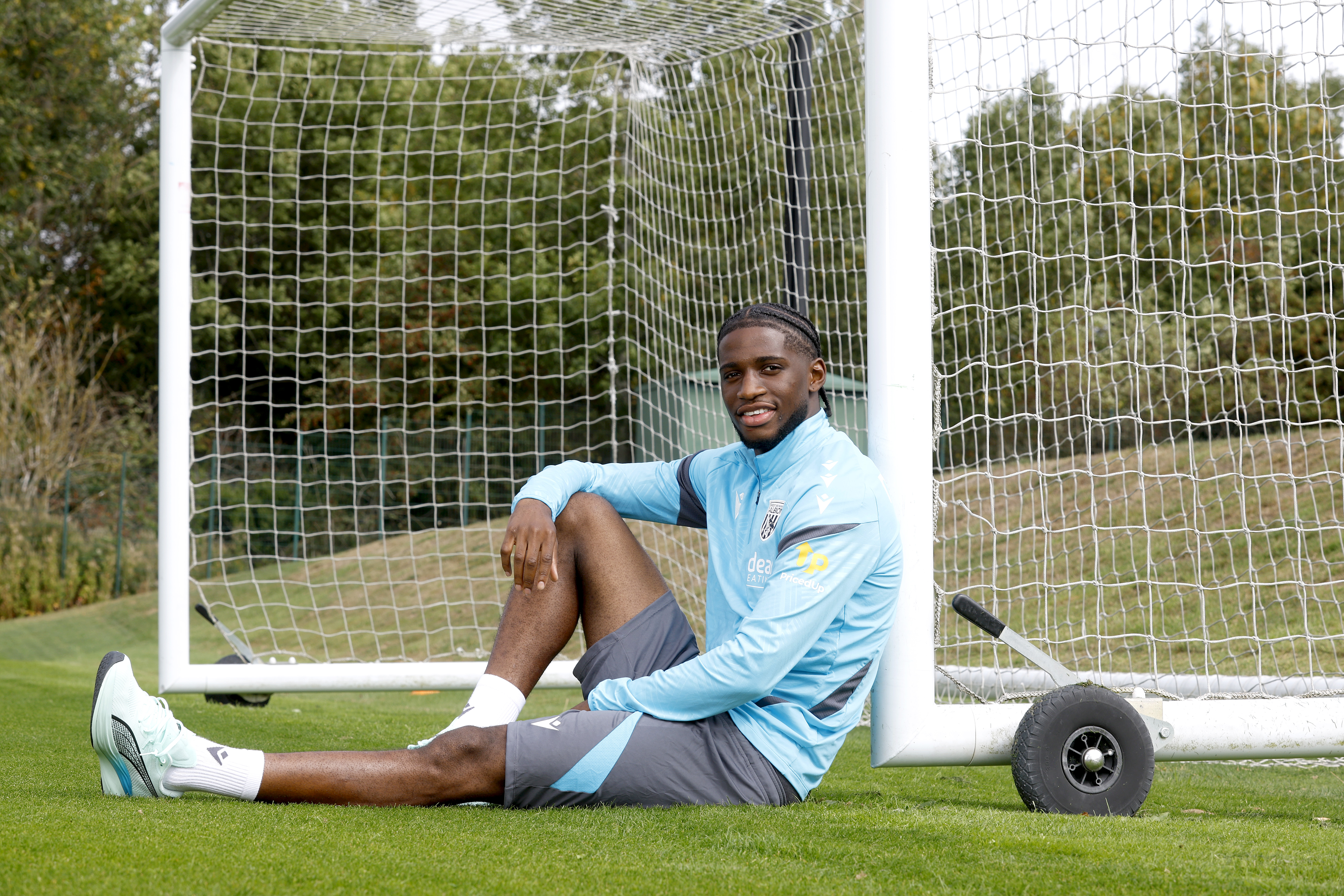Samuel Iling-Junior smiling at the camera while sat up against a goal post on the training pitch