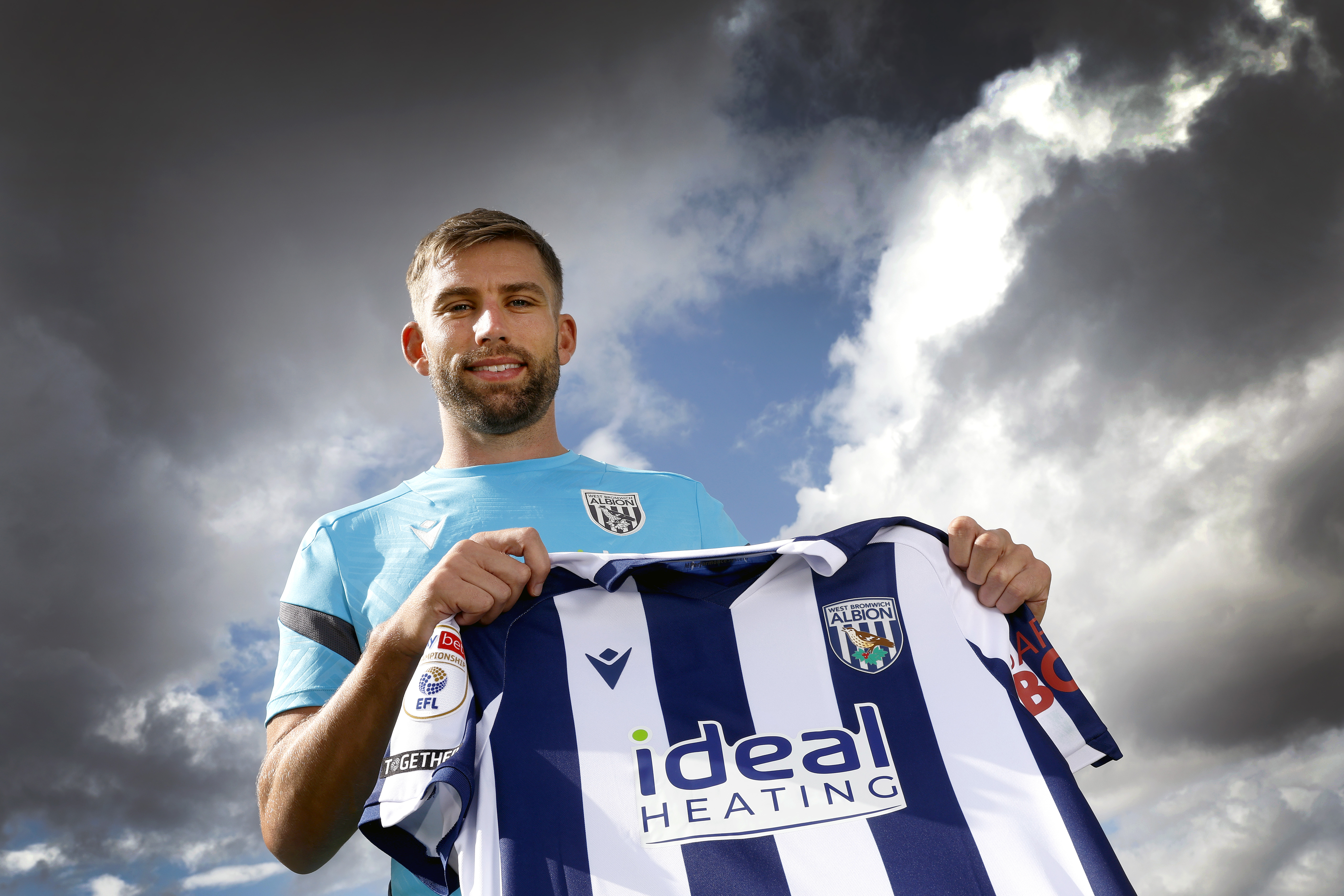 Charlie Taylor smiling at the camera while holding up a home WBA shirt