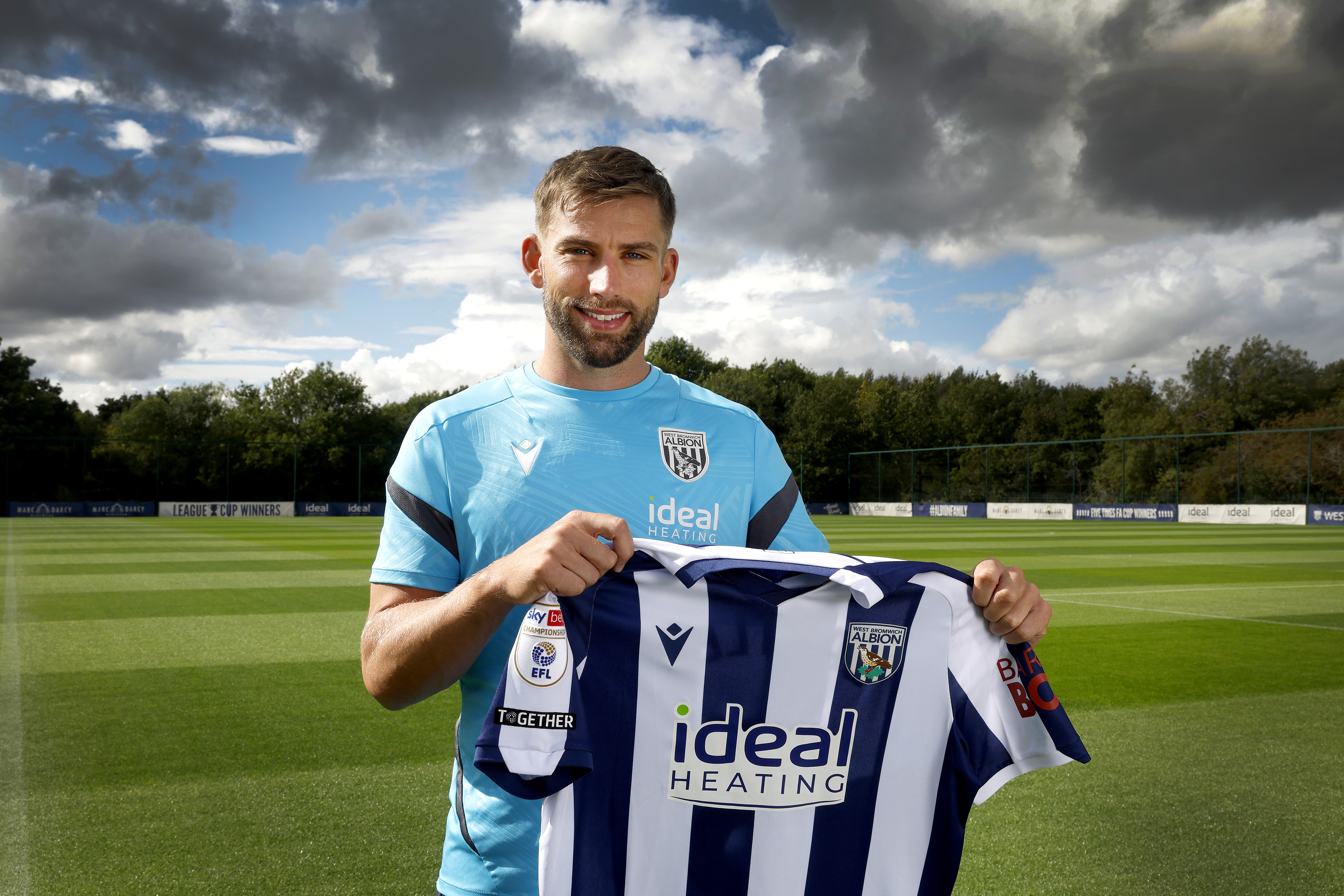 Charlie Taylor smiling at the camera while holding up a home WBA shirt