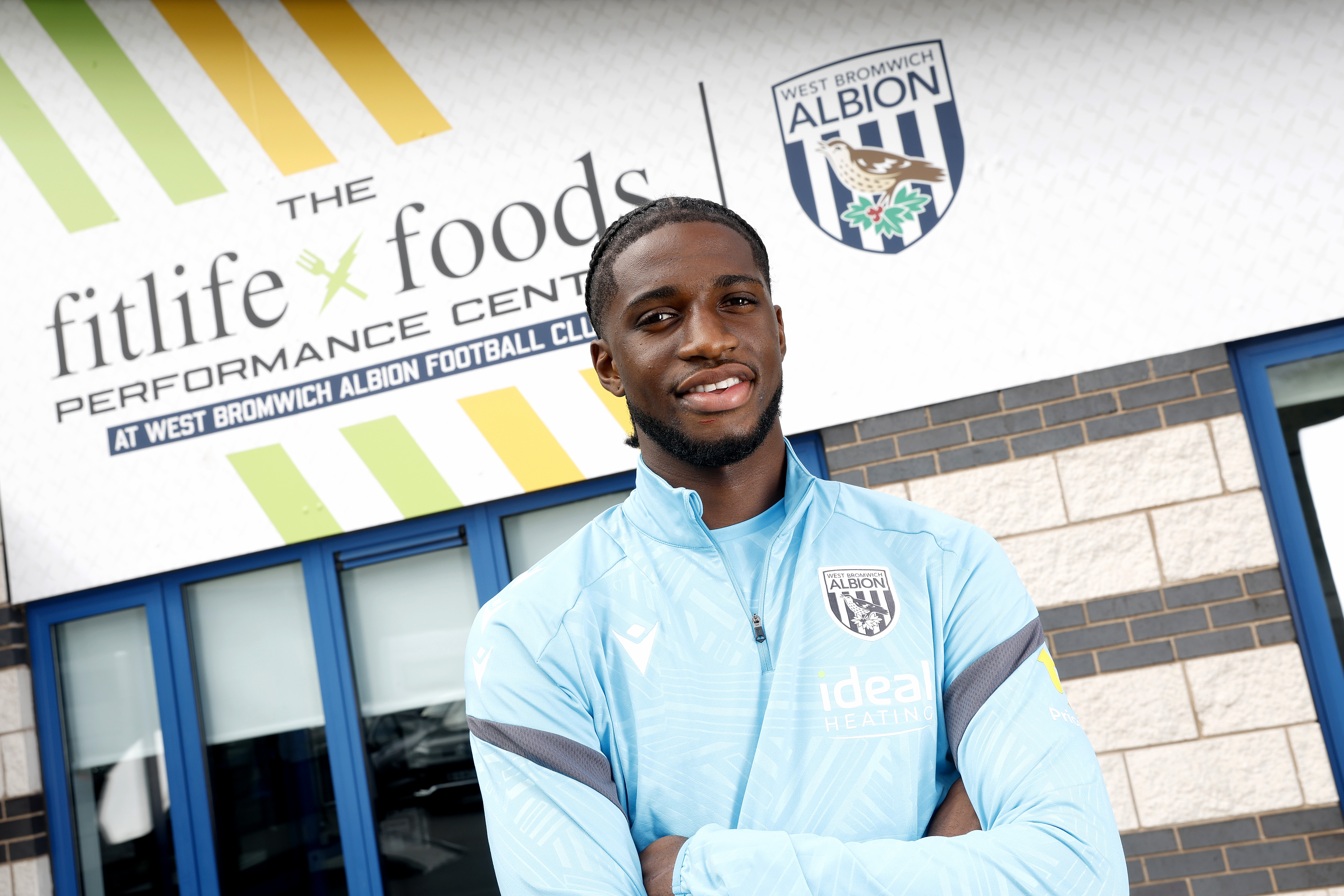 Samuel Iling-Junior smiling at the camera while stood in front of branding outside the training ground