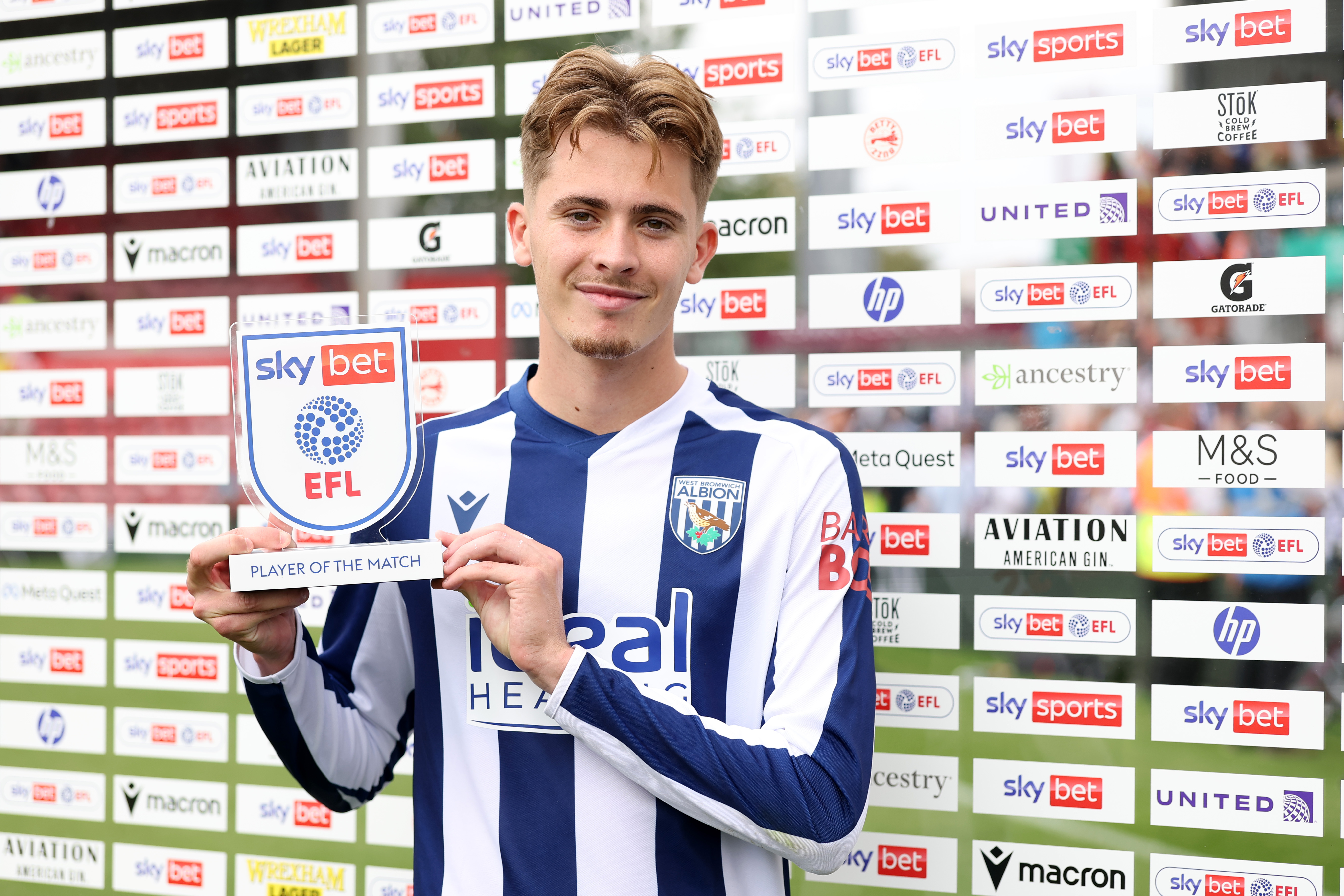 Isaac Price smiling at the camera while holding up a Man of the Match trophy in the home kit 