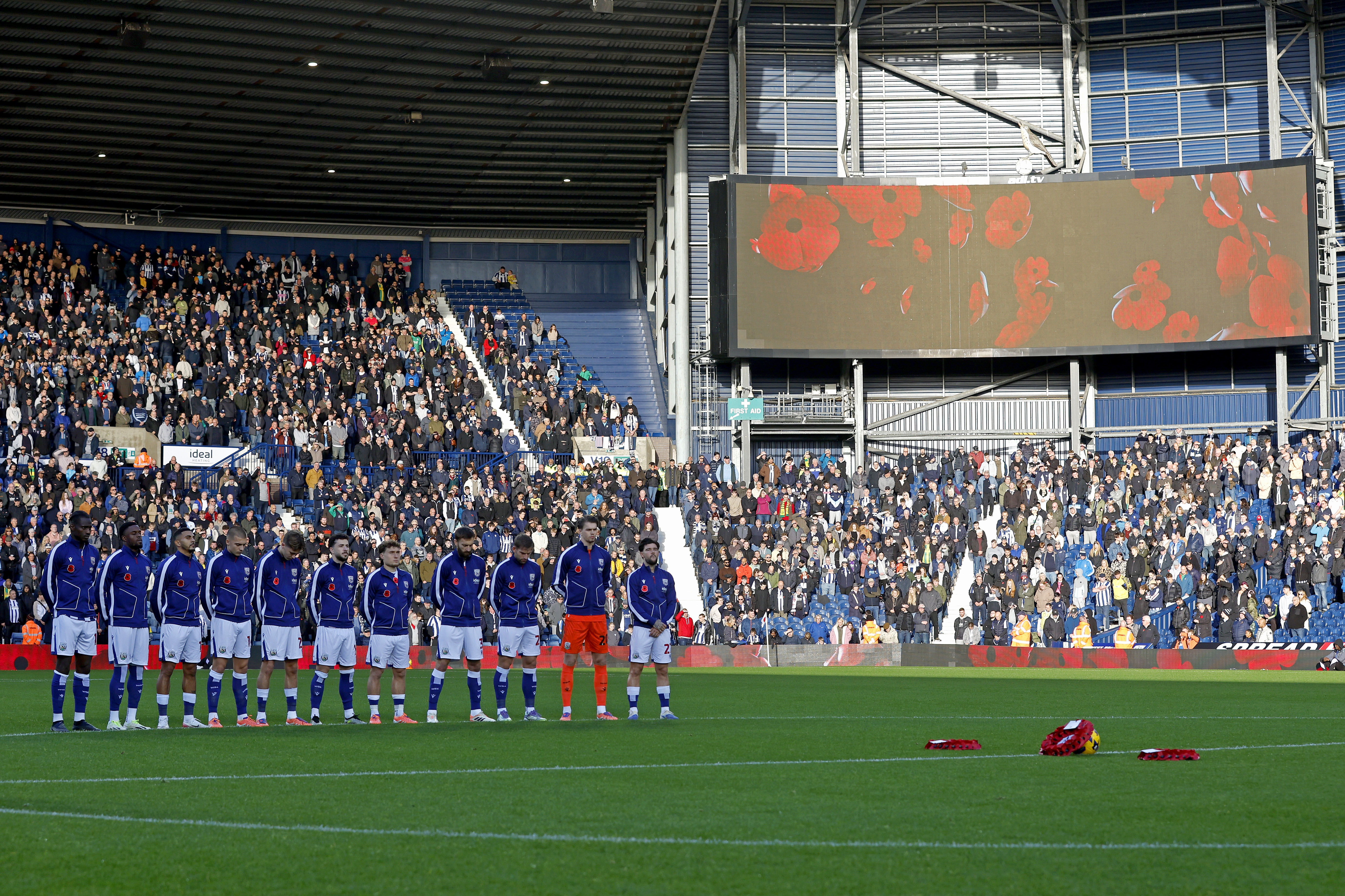 Albion players in a line on the centre circle during a silence with poppies on the big screen in the background 