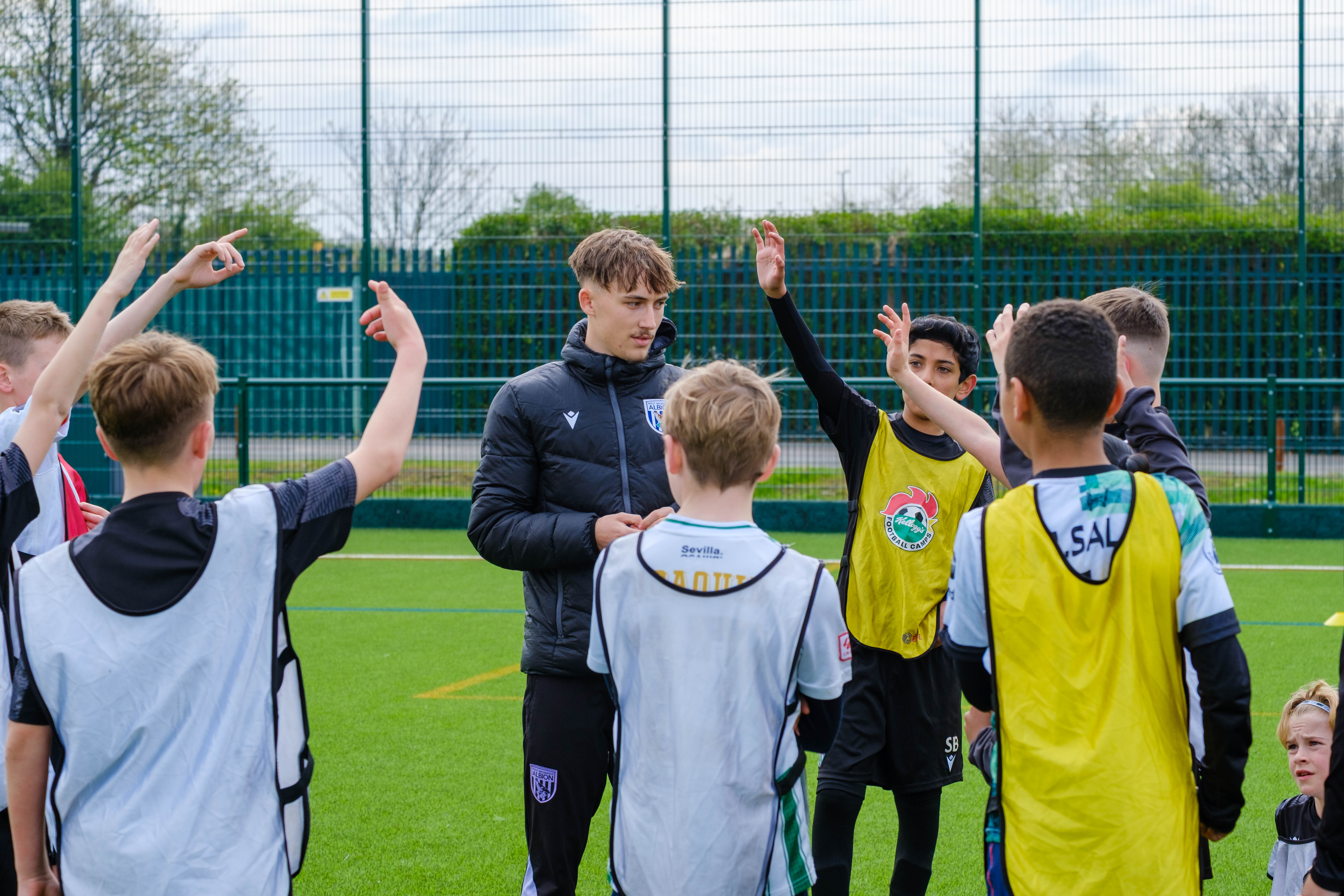 Group of young players, with hands raised, standing around a young coach. 