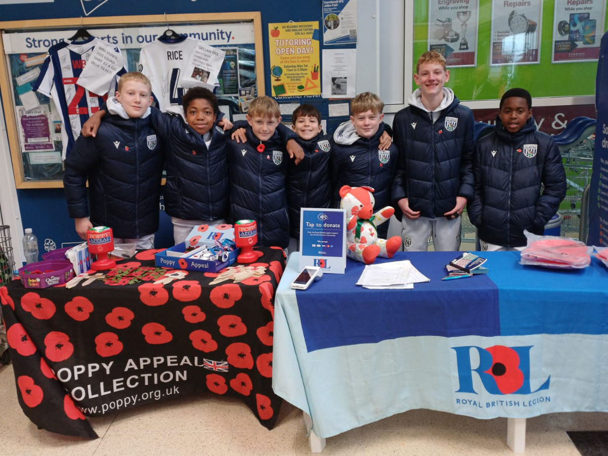 U12 academy players pose for a photo in front of tables with poppies on during a Christmas Truce challenge at Tesco 