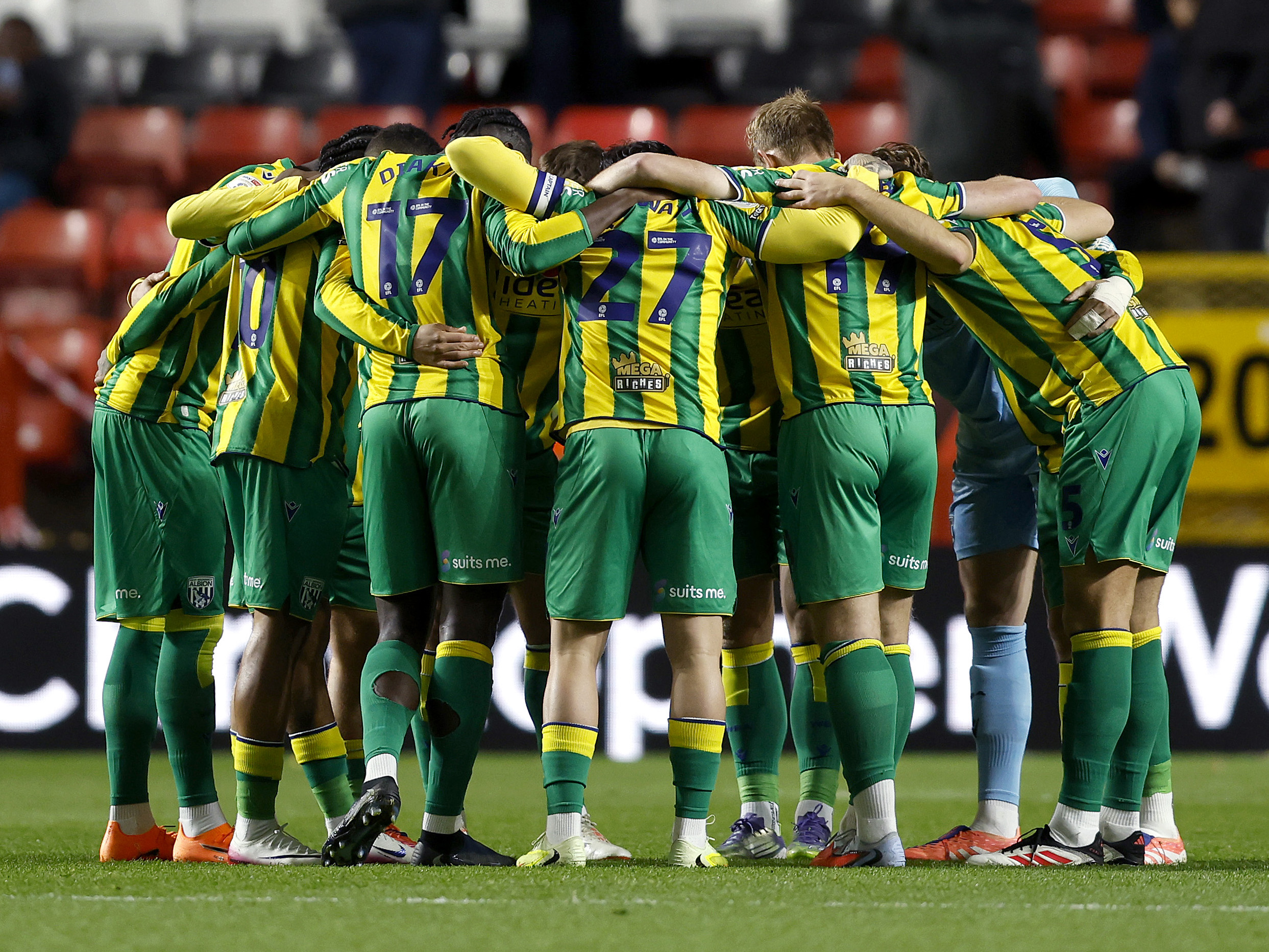 Albion's XI in a huddle in the green and yellow kit at Charlton