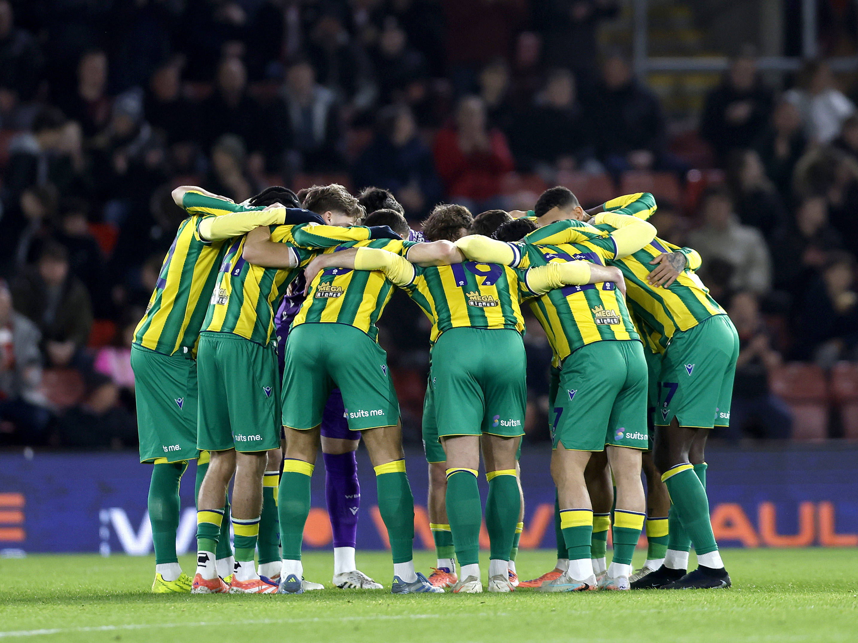 WBA in a team huddle in the green and yellow away kit 