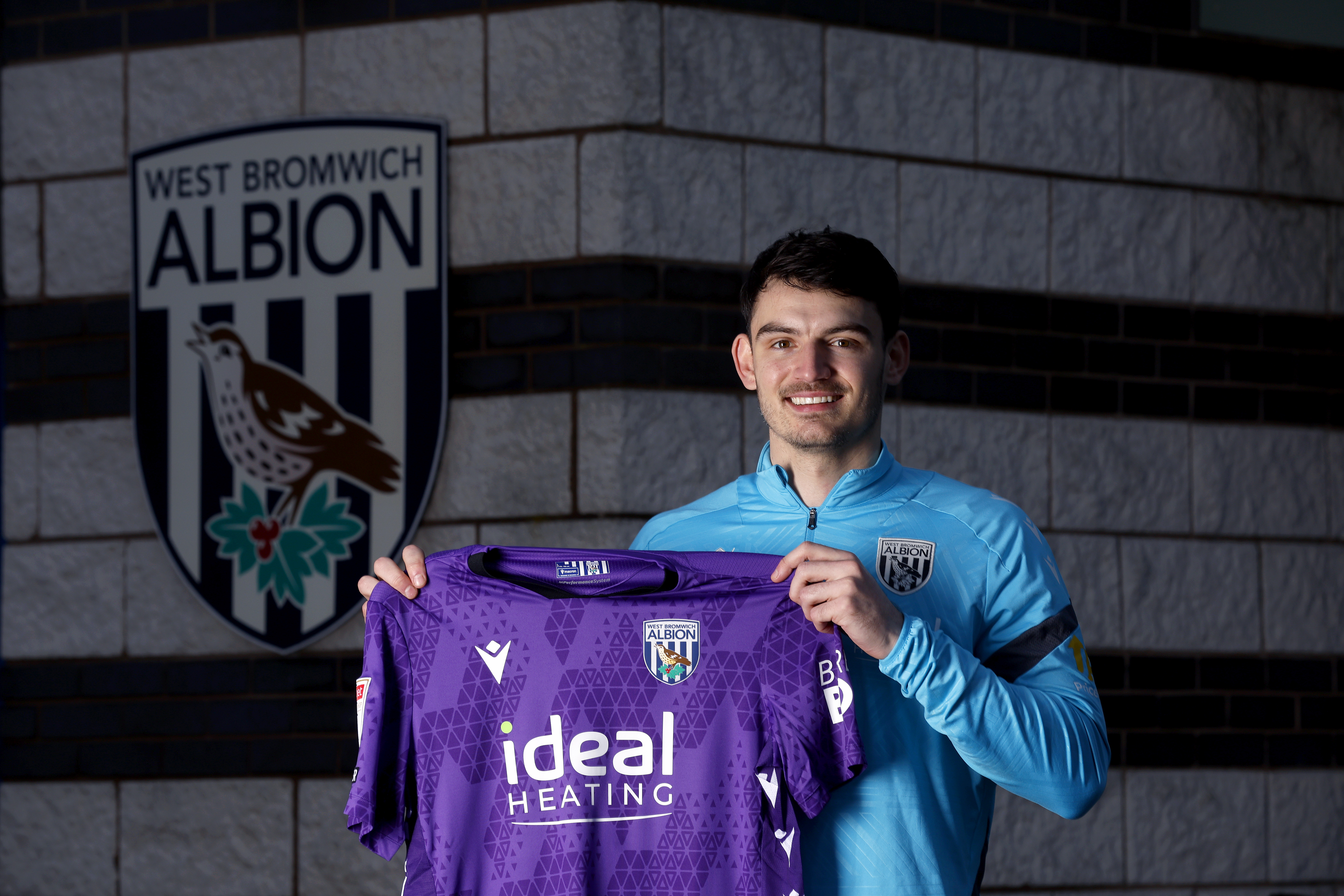 Max O'Leary smiling at the camera while holding up a home WBA GK shirt 