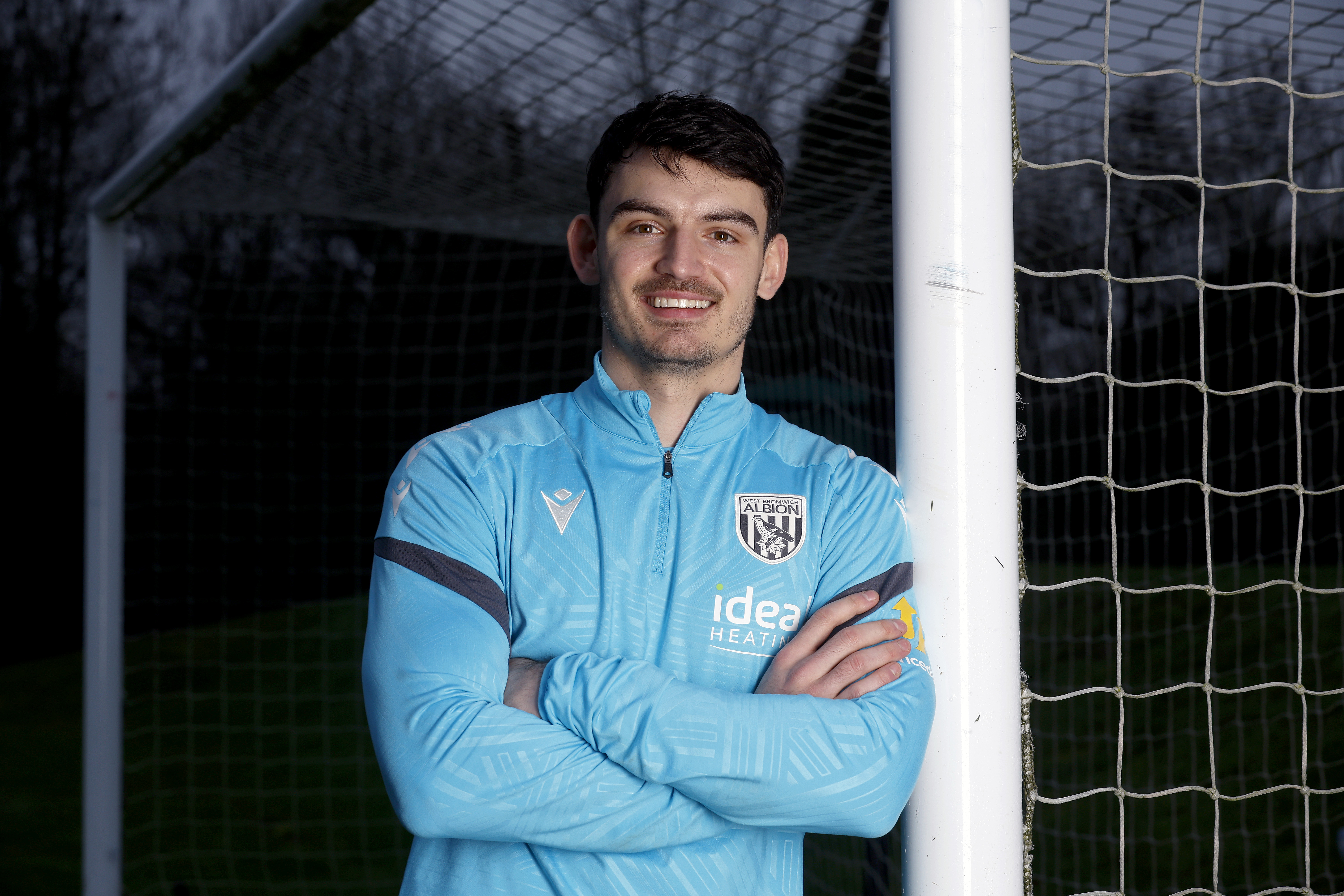 Max O'Leary smiling at the camera while leaning up against a goal post