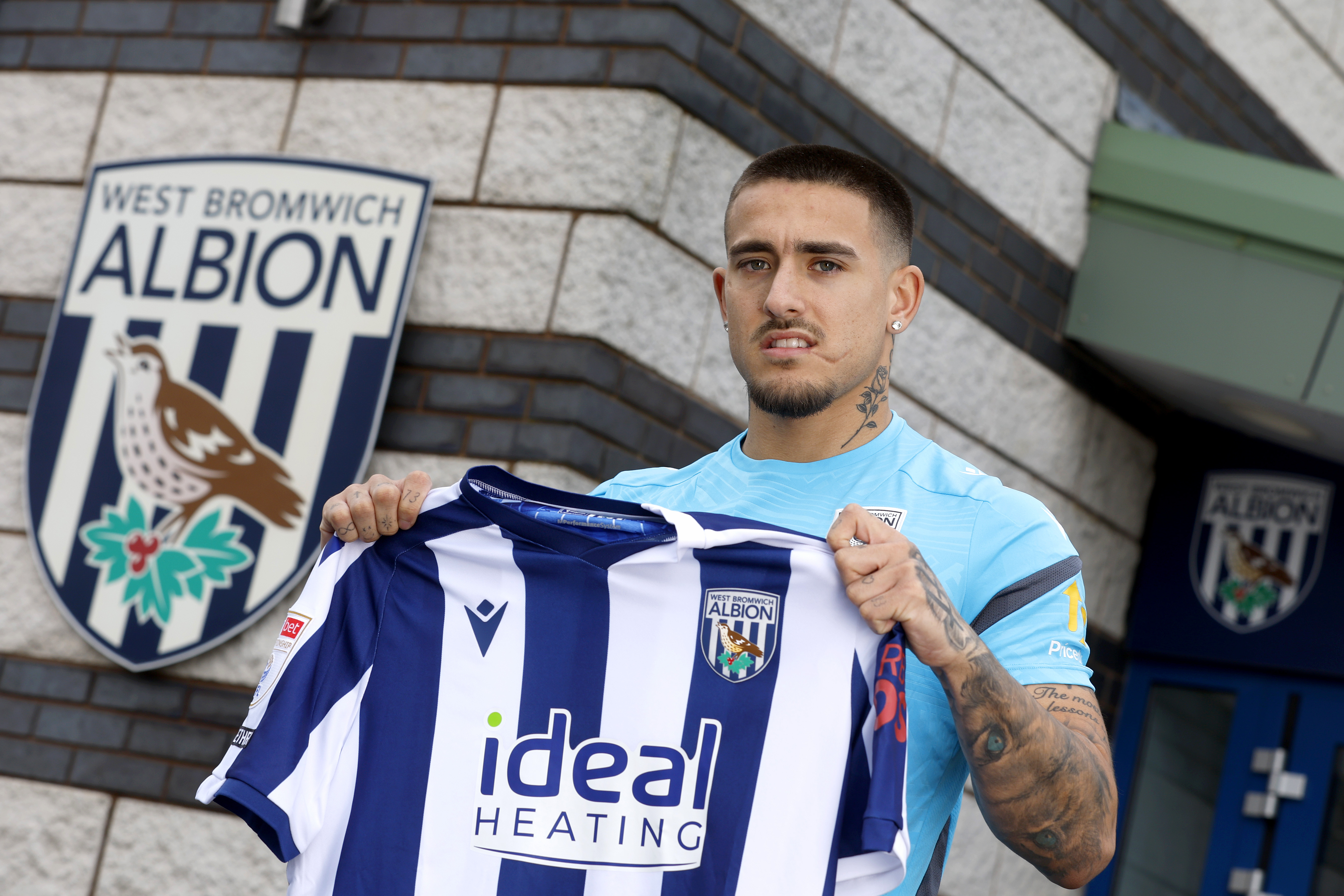 Danny Imray smiling while holding up a home WBA shirt outside the training ground 
