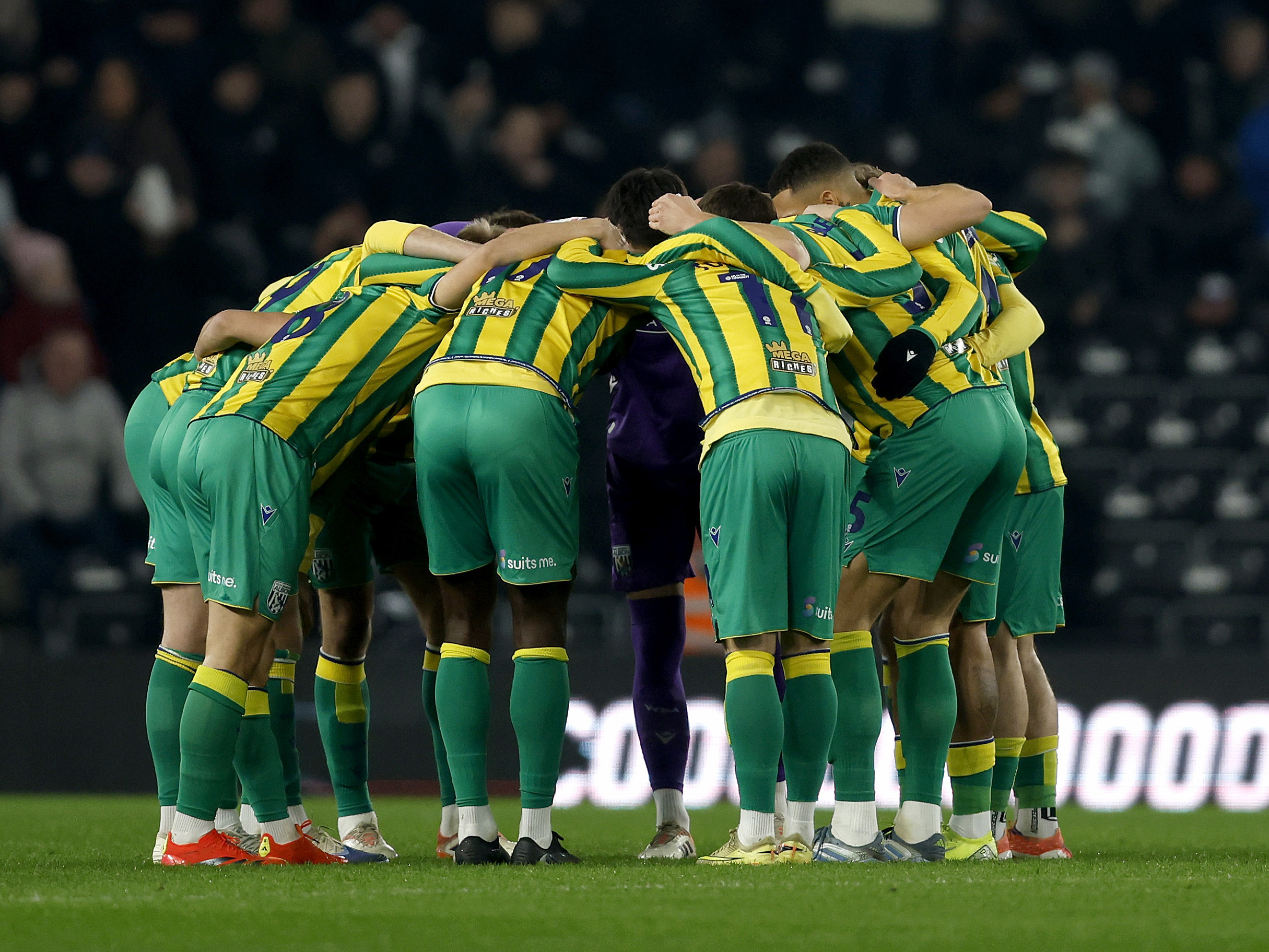 WBA players in a team huddle in the green and yellow away kit before playing Derby at Pride Park