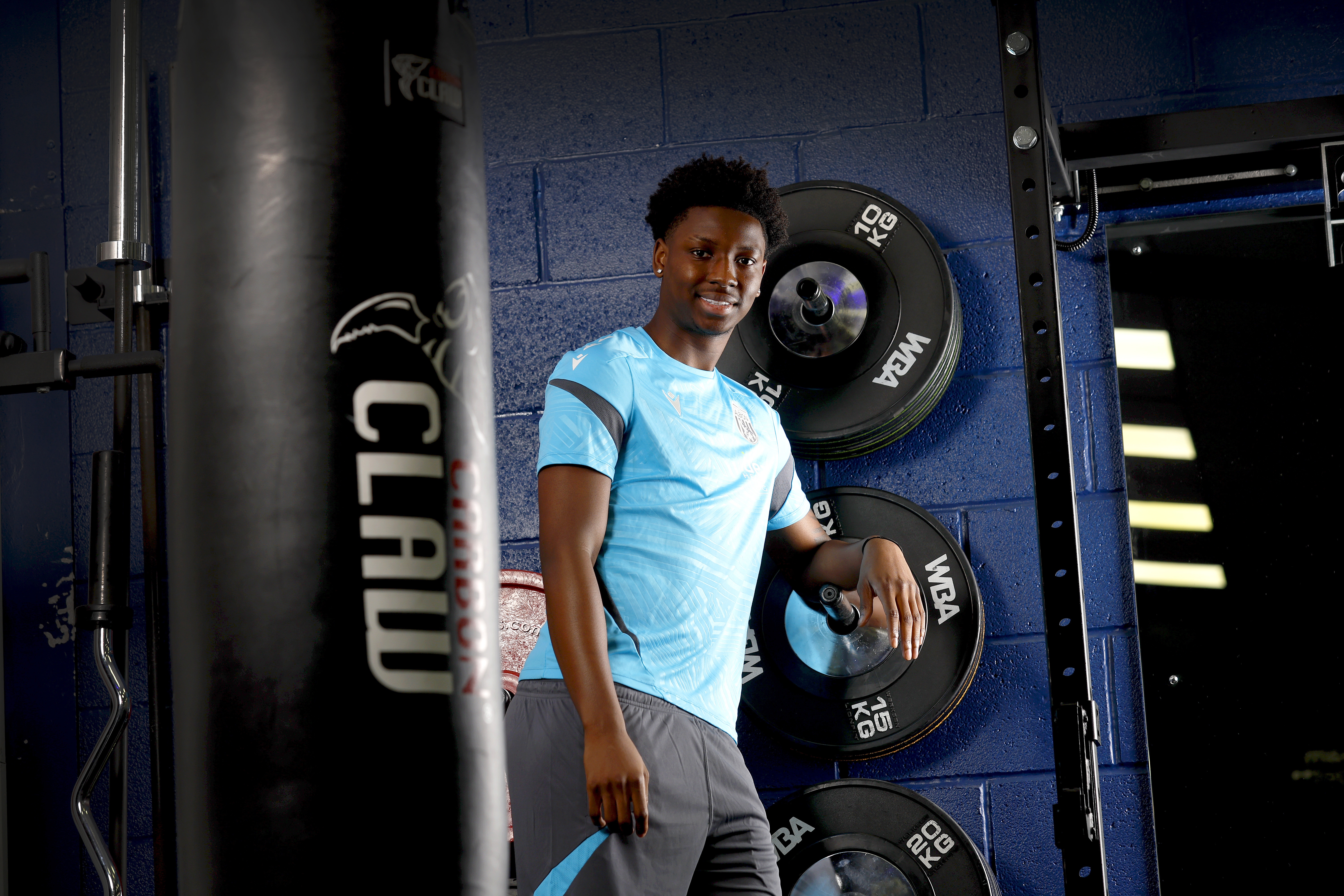 Jamaldeen Jimoh-Aloba smiling at the camera while leaning against equipment in the gym