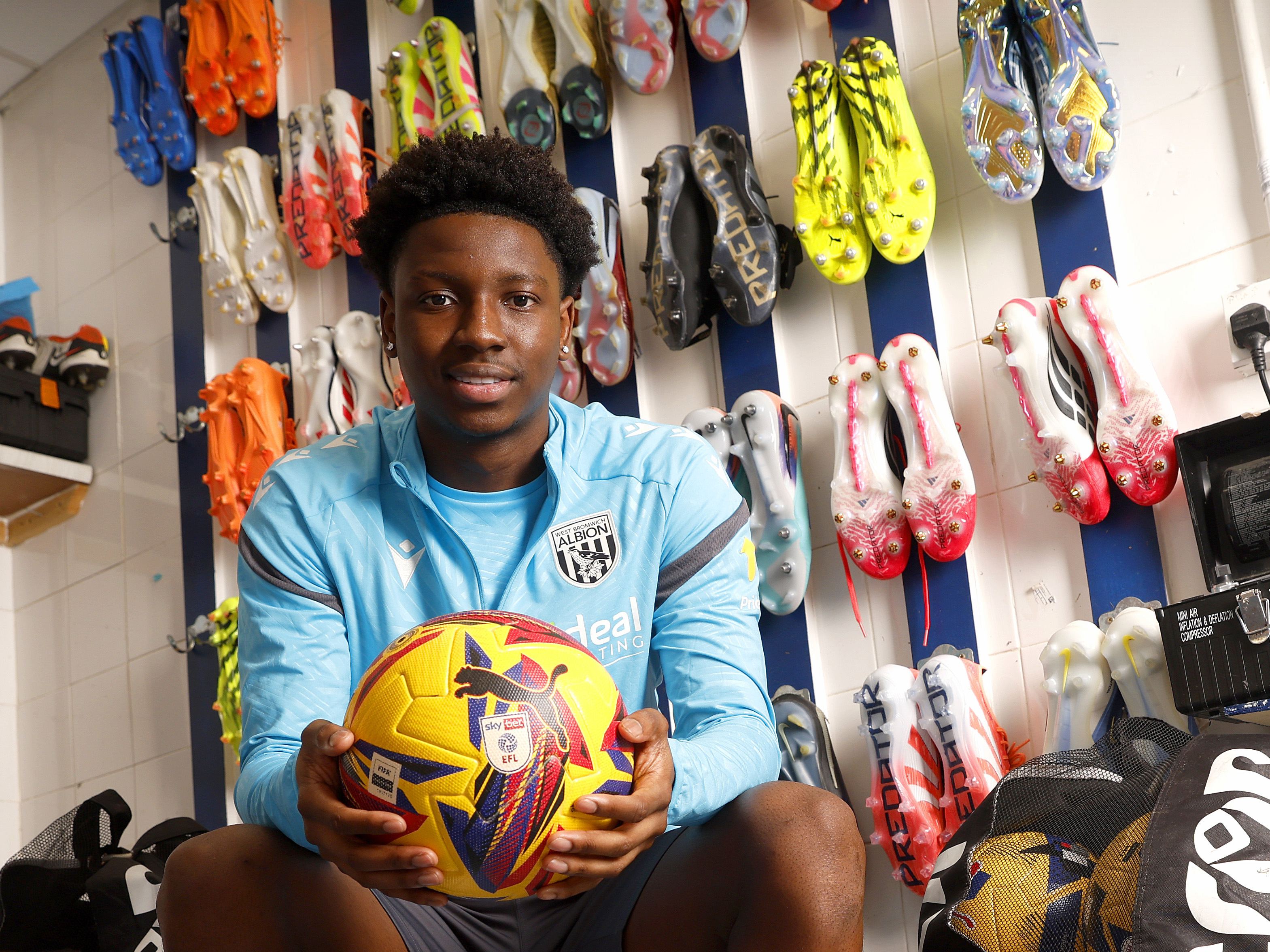 Jamaldeen Jimoh-Aloba smiling at the camera while holding a ball in the boot room