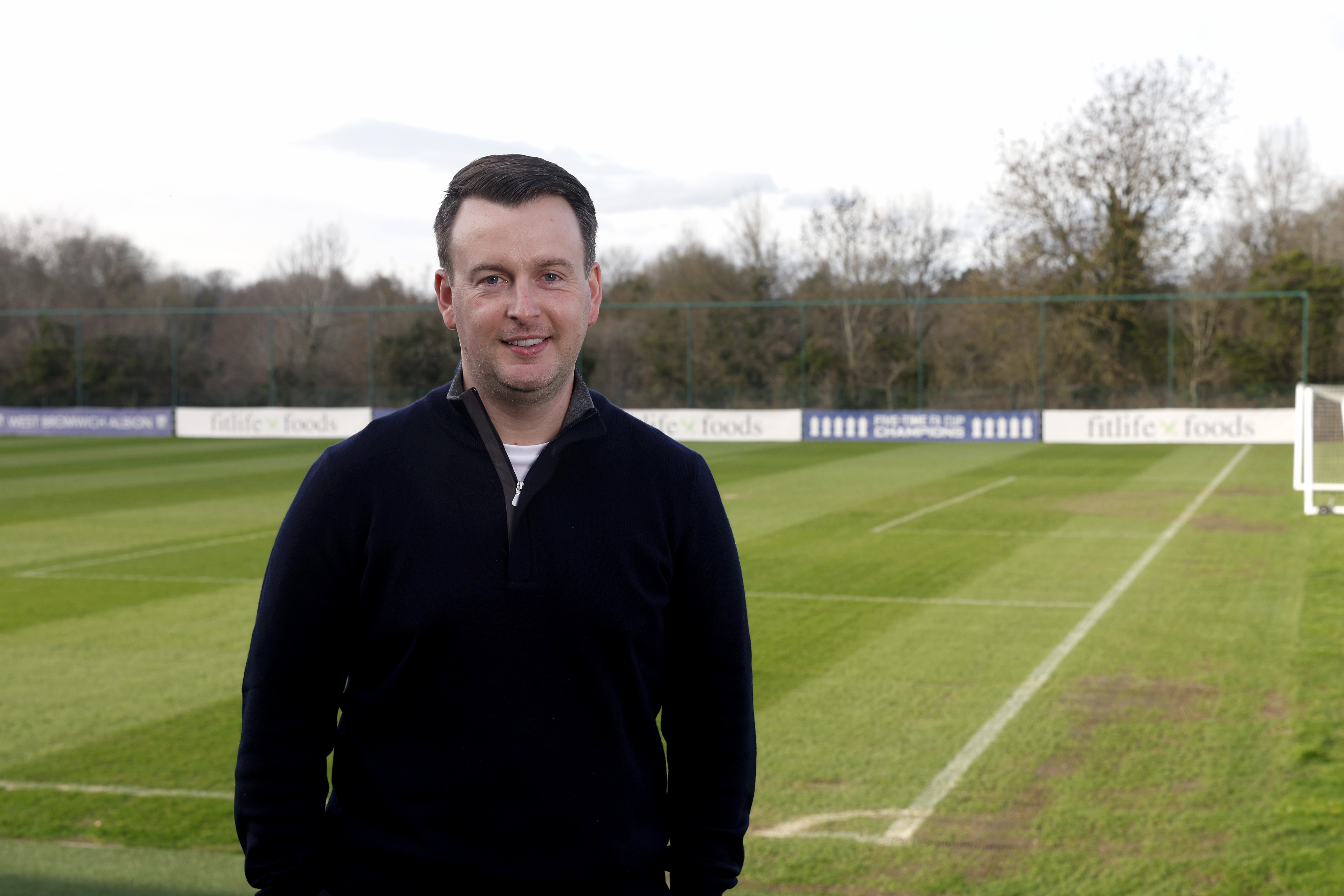 Dominic Price smiling at the camera with a pitch in the background 