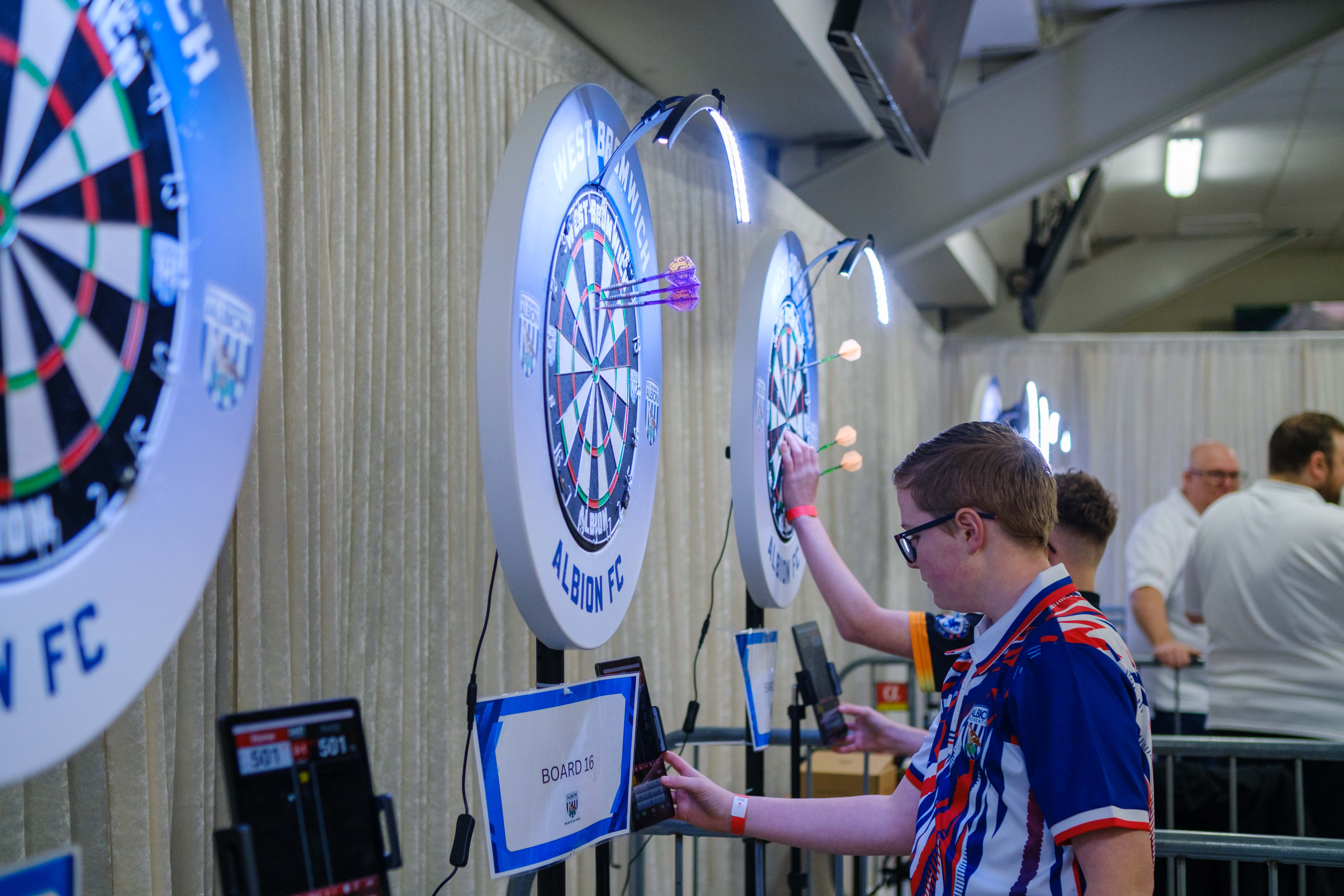 Junior player inputting his score on a tablet with dartboards in the background