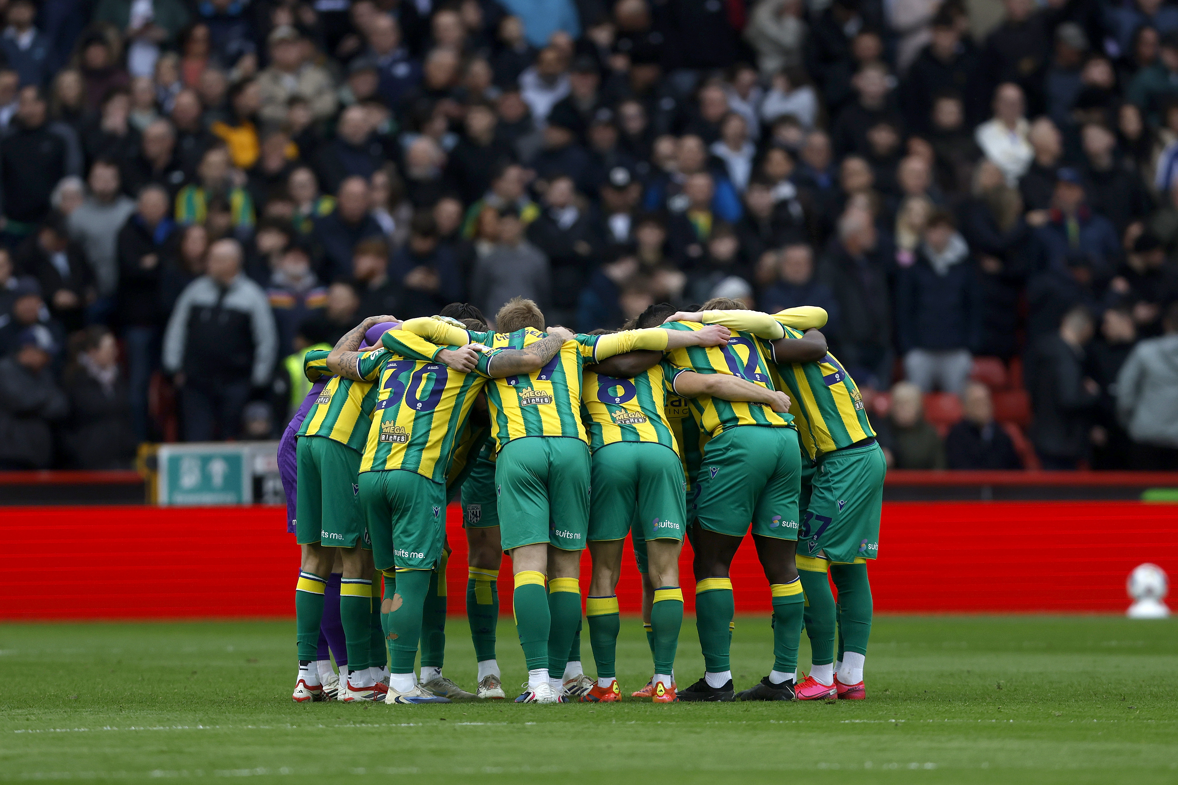 WBA players in the green and yellow away kit in a pre-match huddle before taking on Sheffield United 