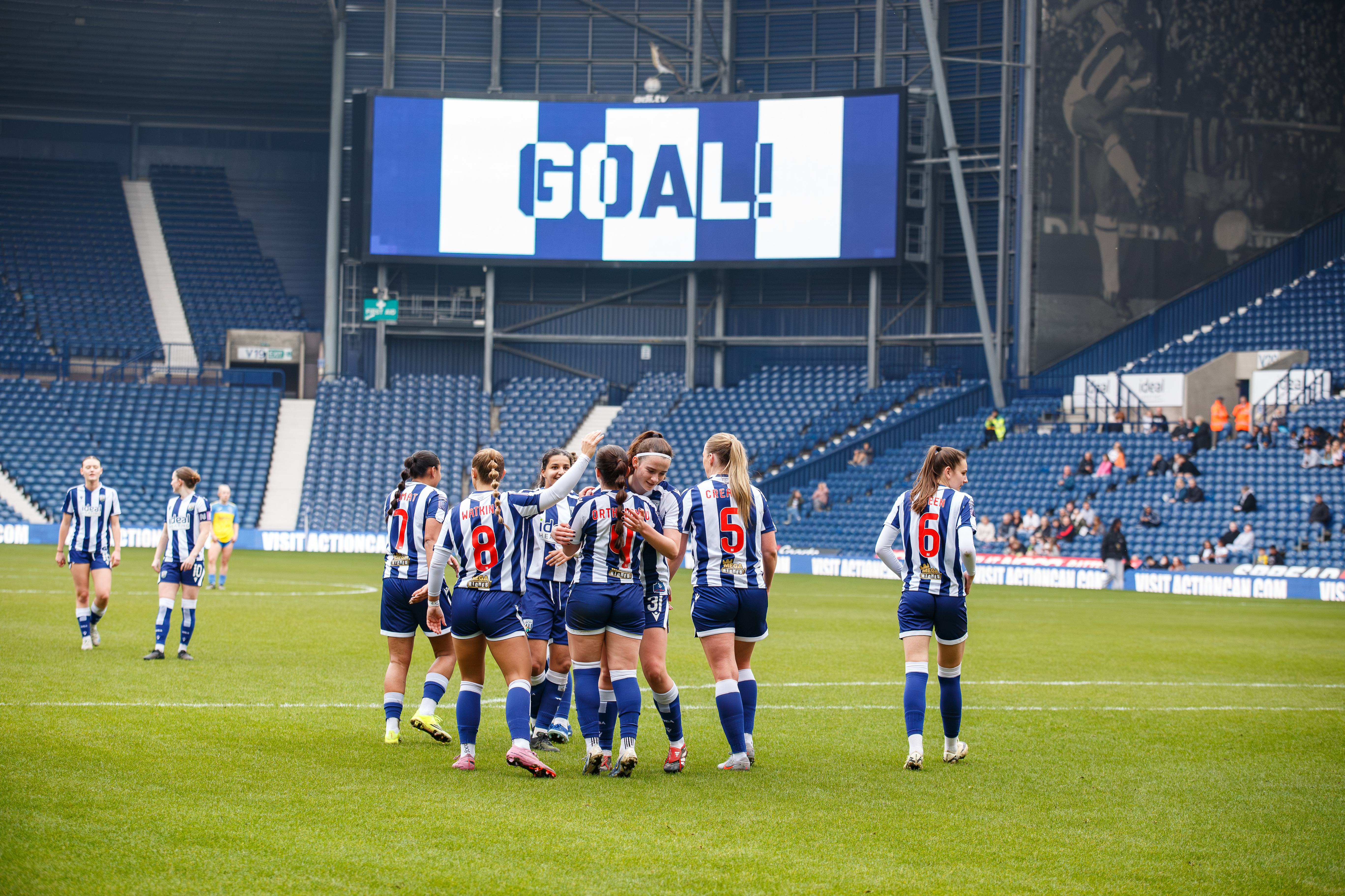 Albion Women players celebrate a home goal at The Hawthorns with 'GOAL' written on the big screen in the background 