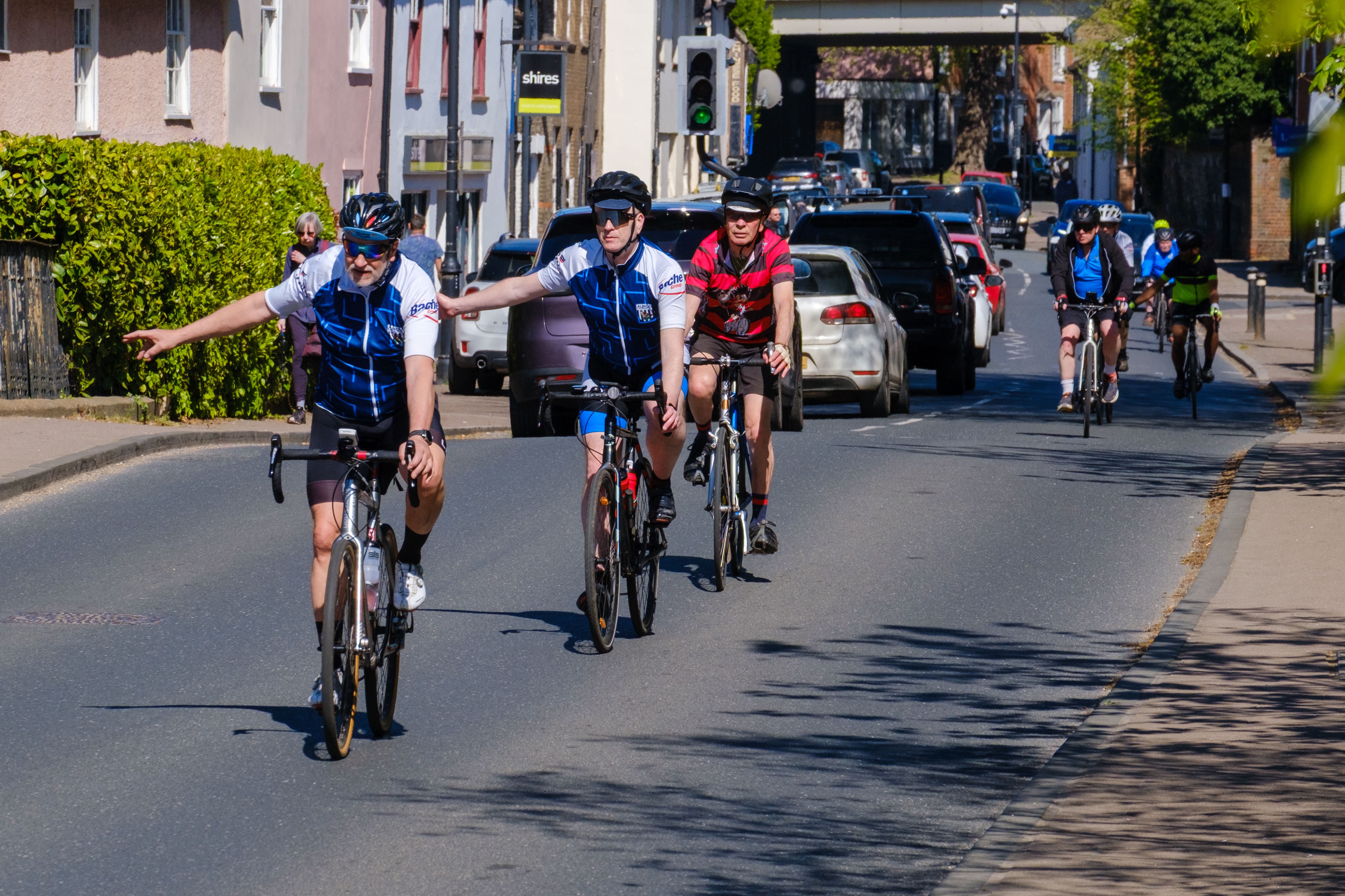 Three cyclist signalling to turn right on a high street.