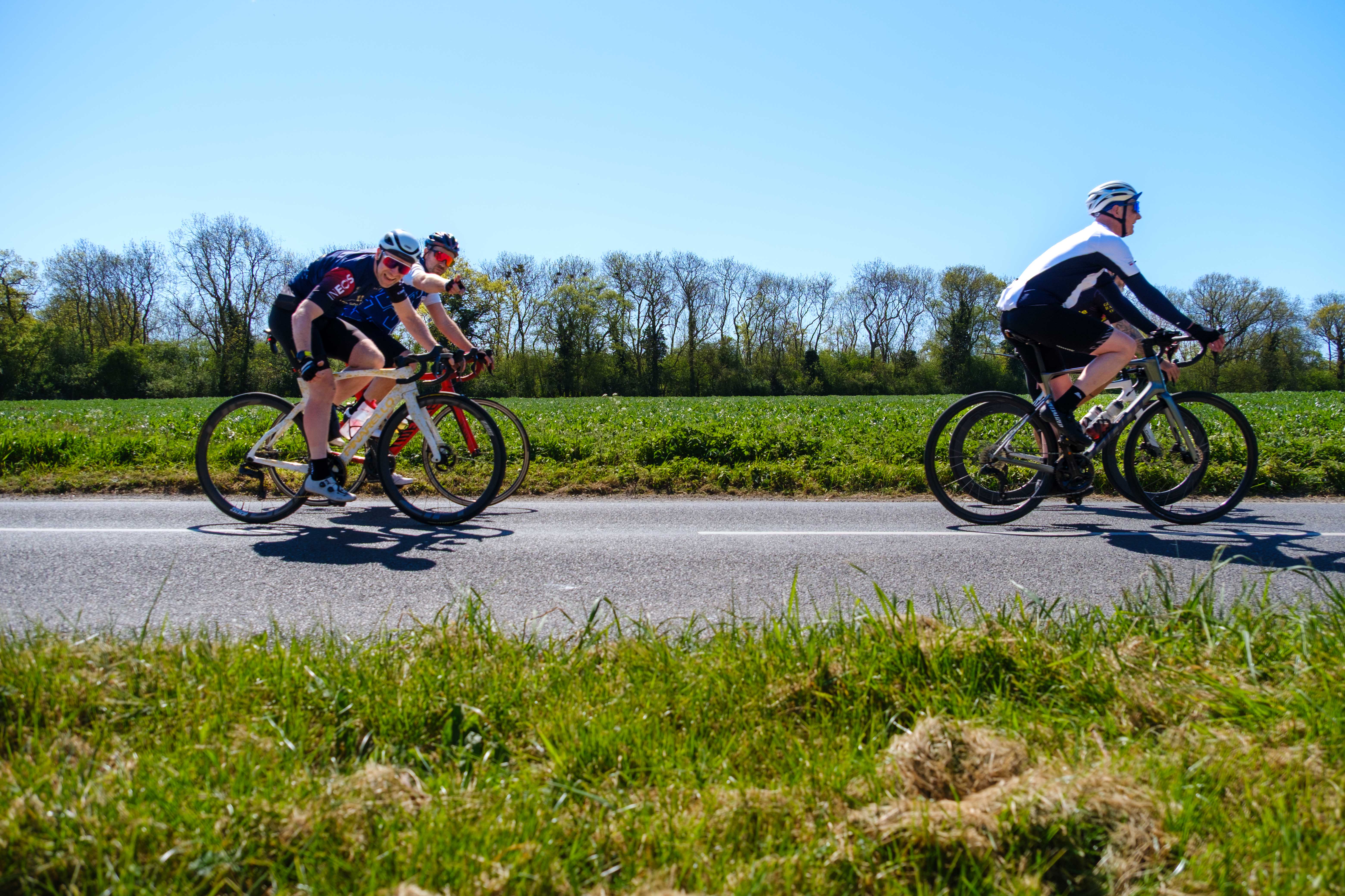 Cyclists pointing towards the camera as they cyclist along a country road.