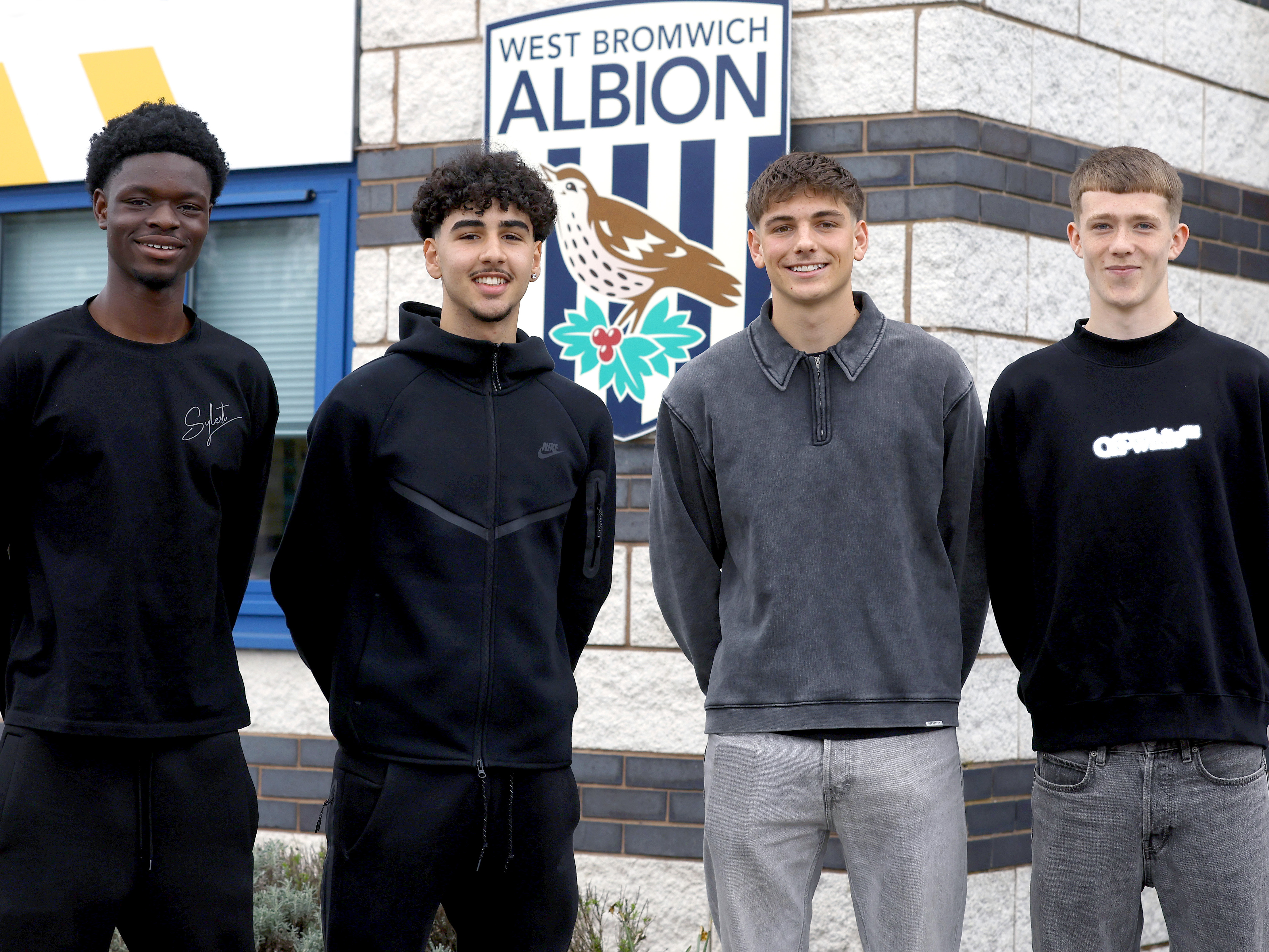 Abdul Abudu, Adam Letlat, Charlie Blackshields and Ryan Colesby smile at the camera in front of the training ground 