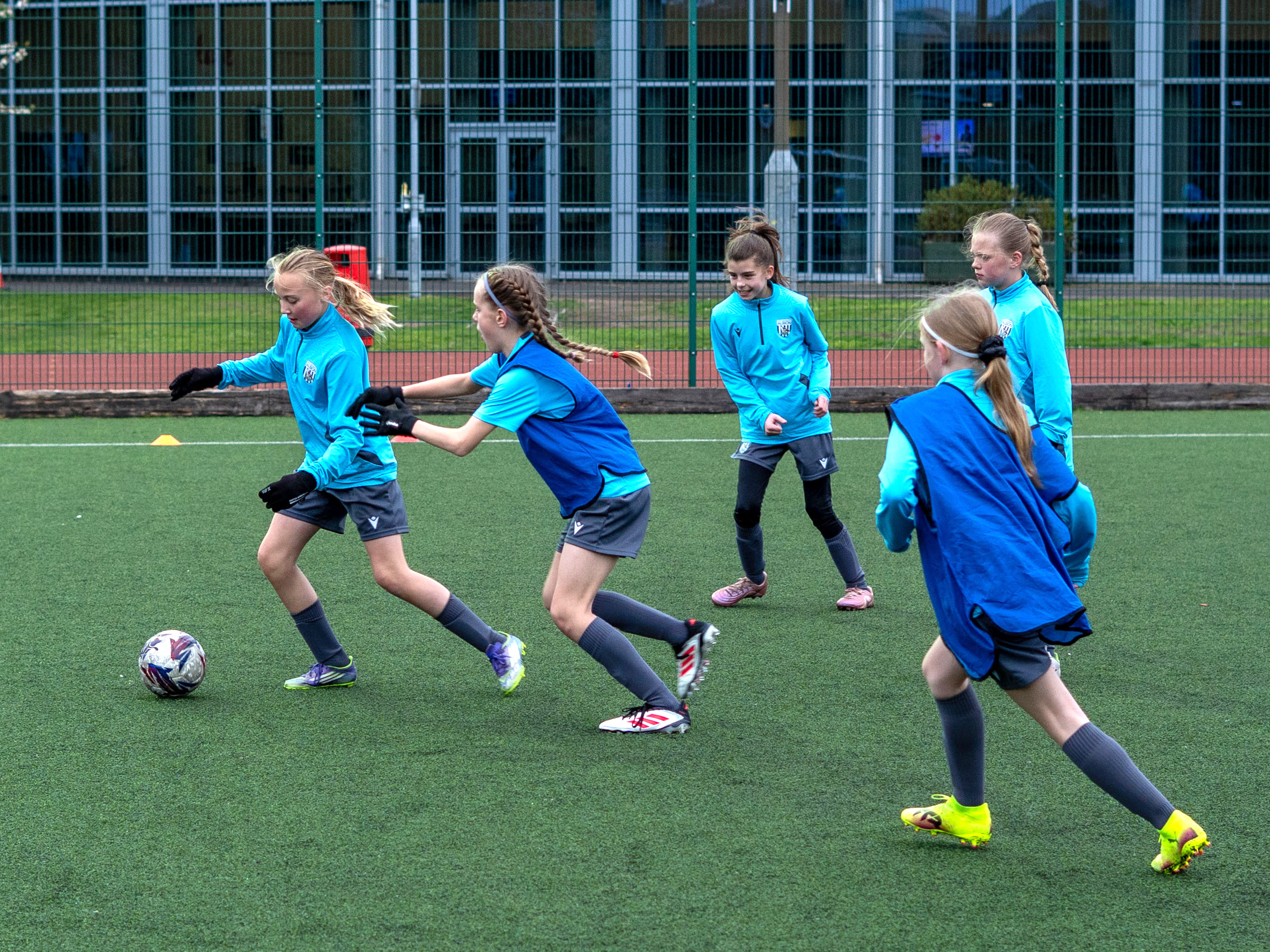 Players dribbling the ball with players in bibs chasing.