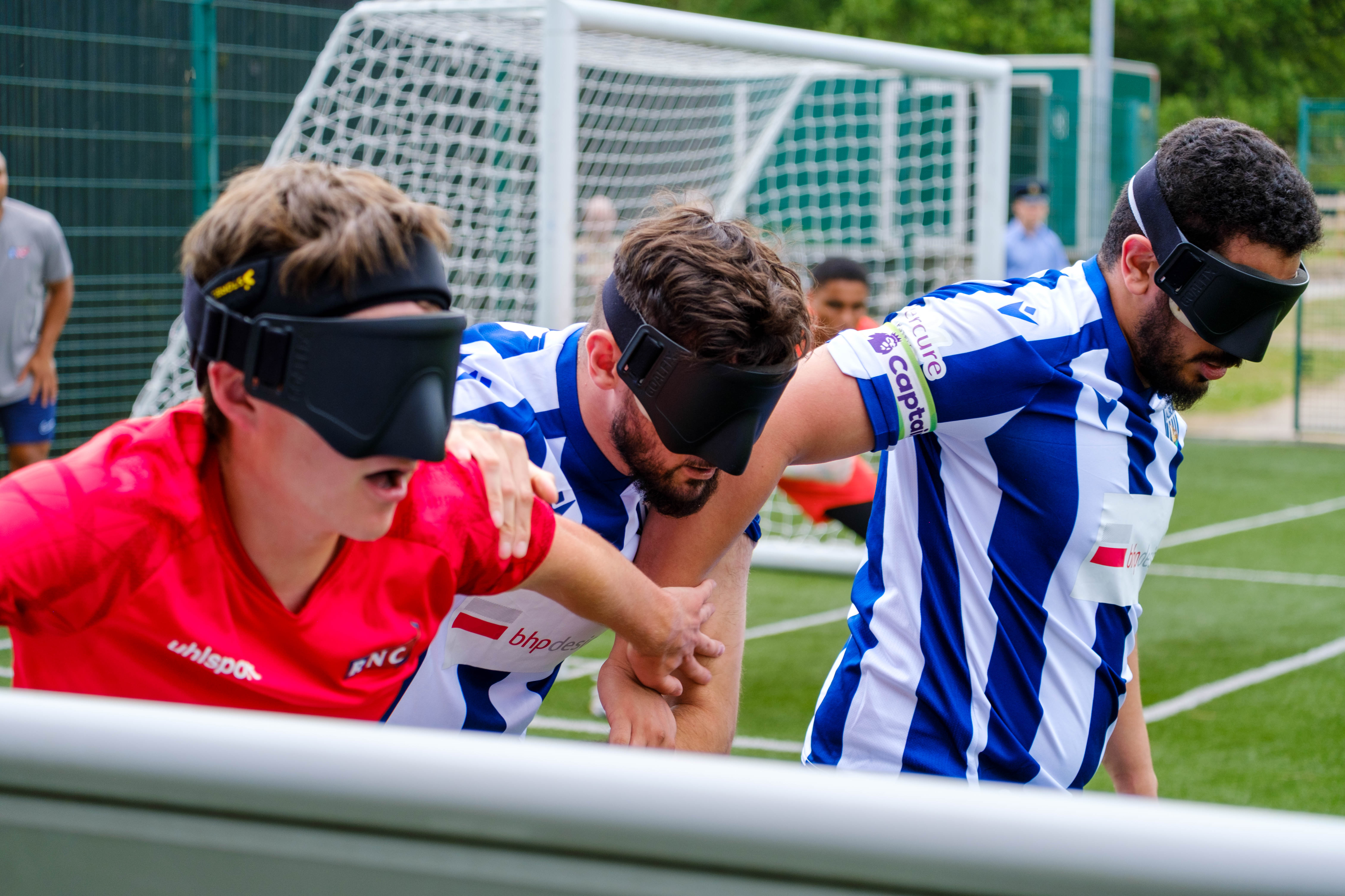 Close-up of Mo Ahmed, Kieran Clarke & RNC player attempting to gain the ball next to the pitch boards.